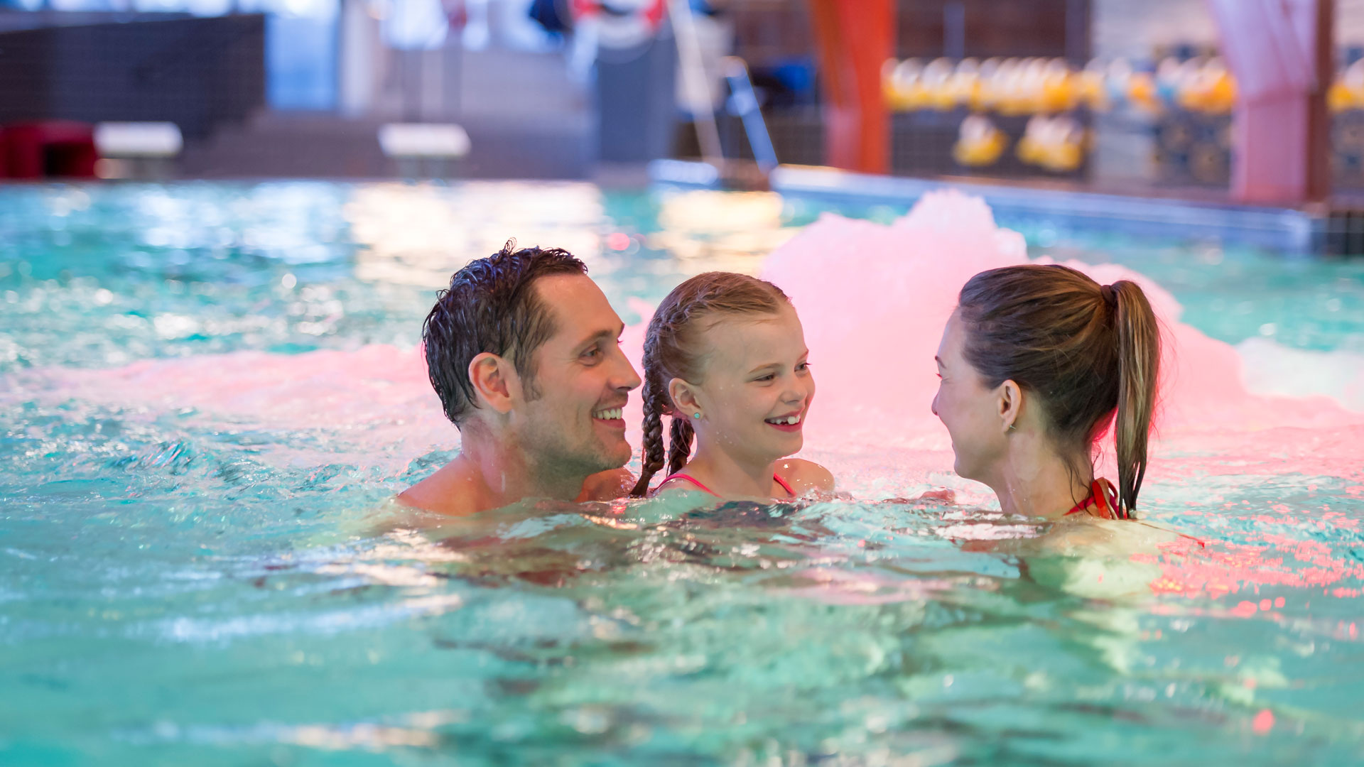 A family enjoys an indoor pool, smiling and swimming together