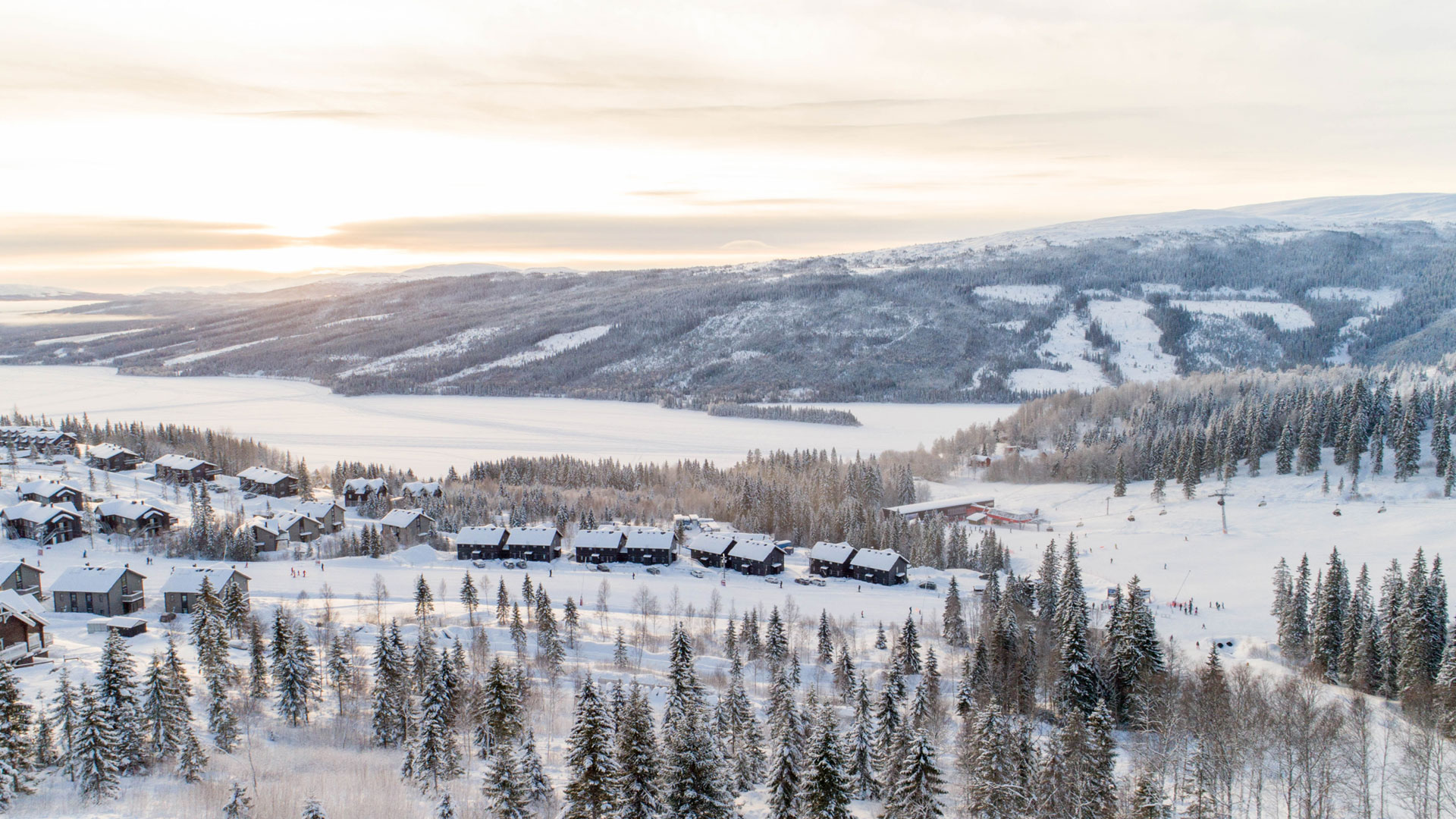 Vinterlandskab i Åre, Sverige, med snedækkede hytter, skov og bjerge i baggrunden på en solrig dag