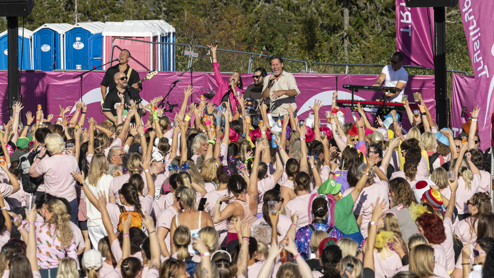 Kvinnor klädda i rosa deltar i ett utomhusevenemang med livemusik, omgivna av glädje och gemenskap