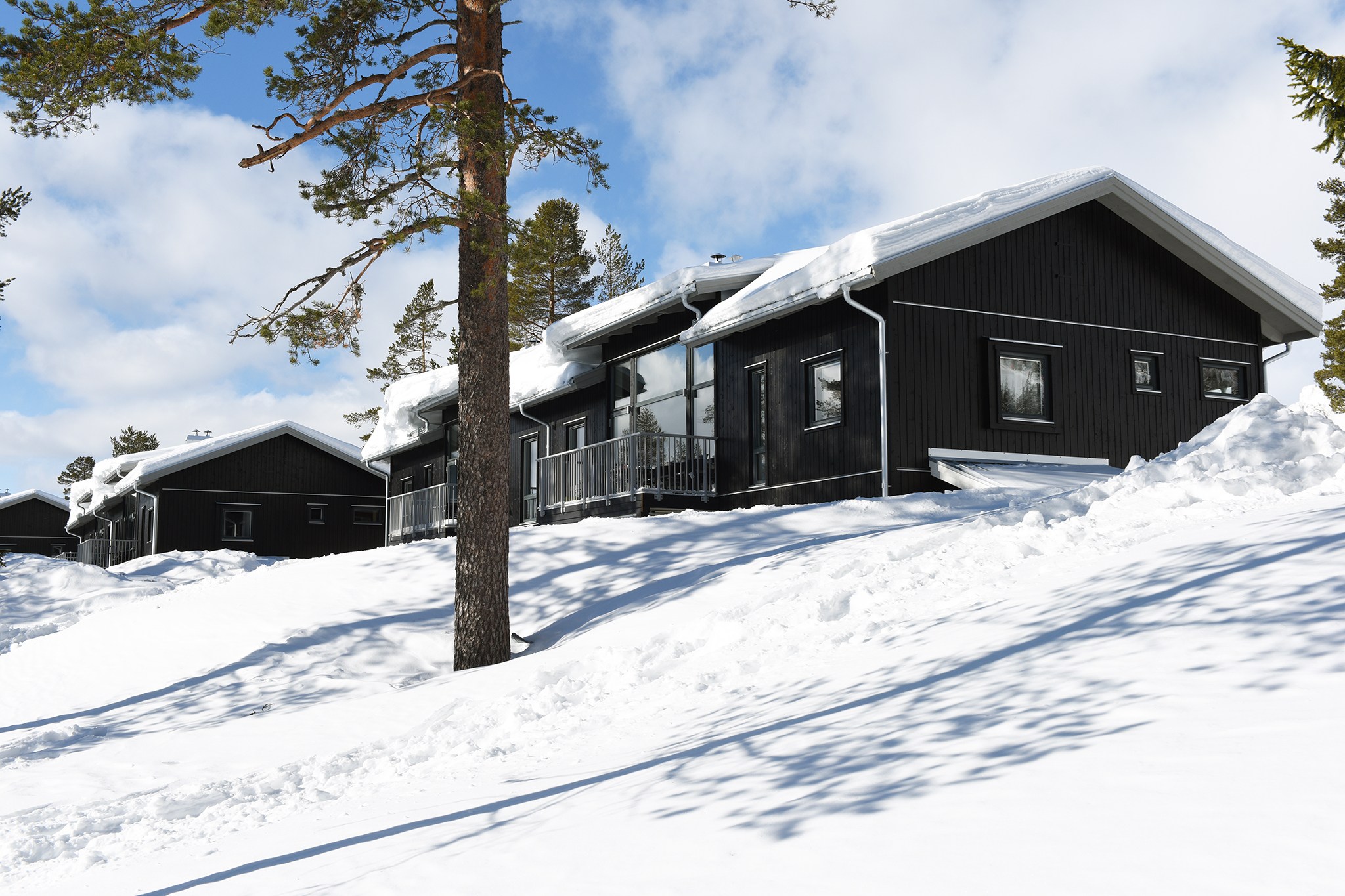 Svart fjällstuga i snötäckt landskap under klarblå himmel i svenska fjällen