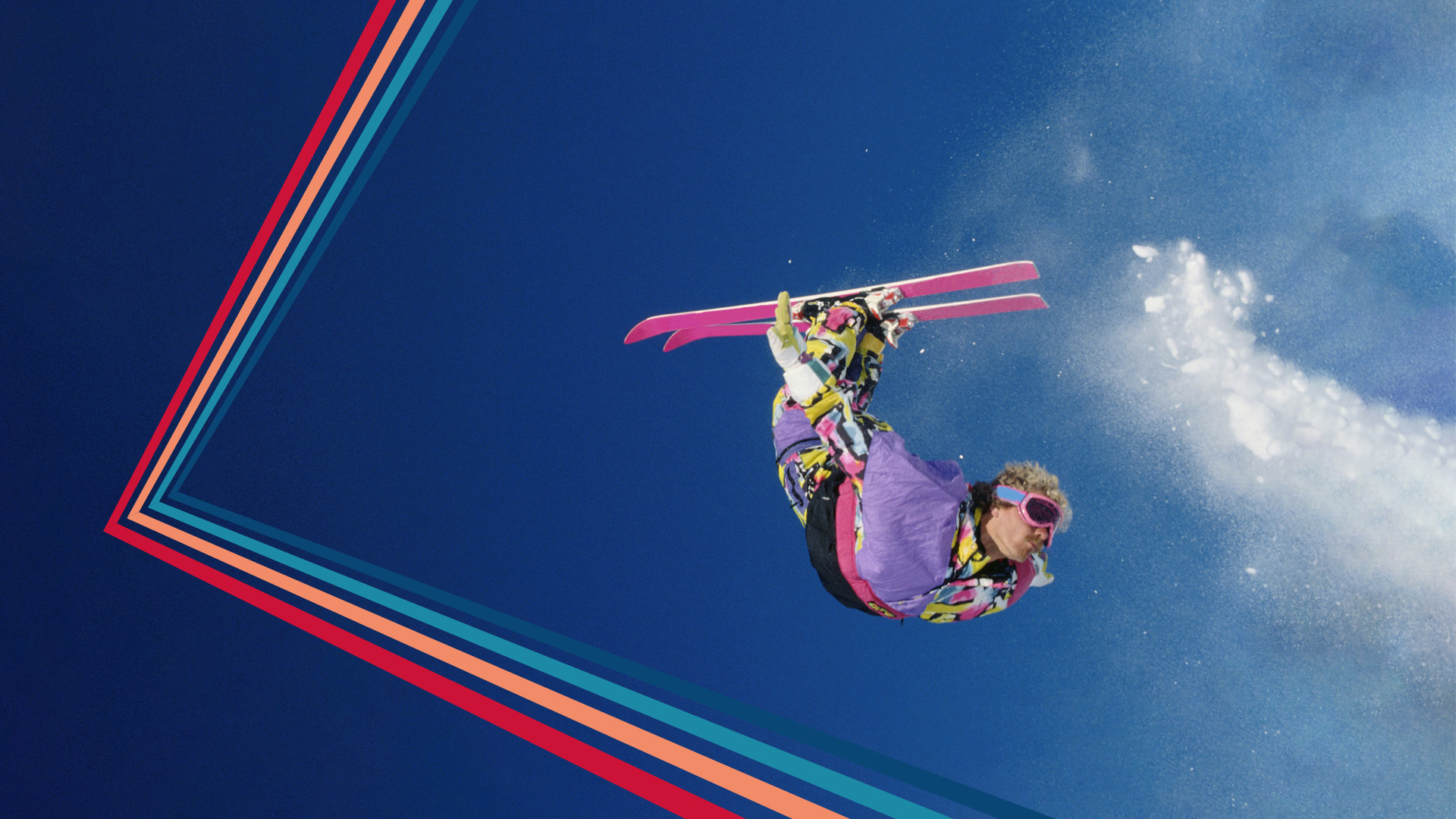 Skiløber i farverigt outfit udfører en spektakulær luftpiruette med en klar blå himmel i baggrunden