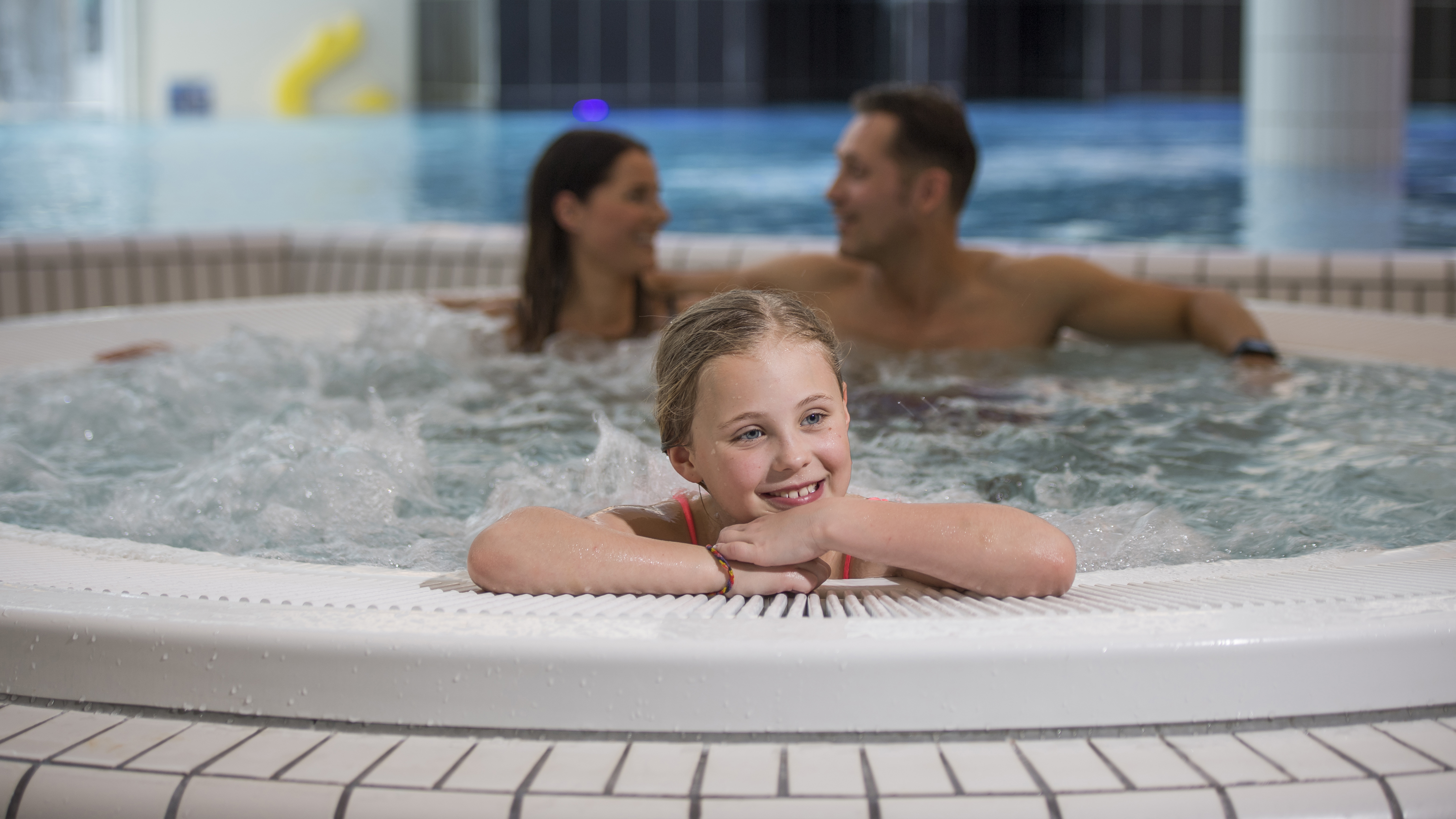 Barn leker i en bubbelpool medan två vuxna sitter i bakgrunden i ett spa eller badhus