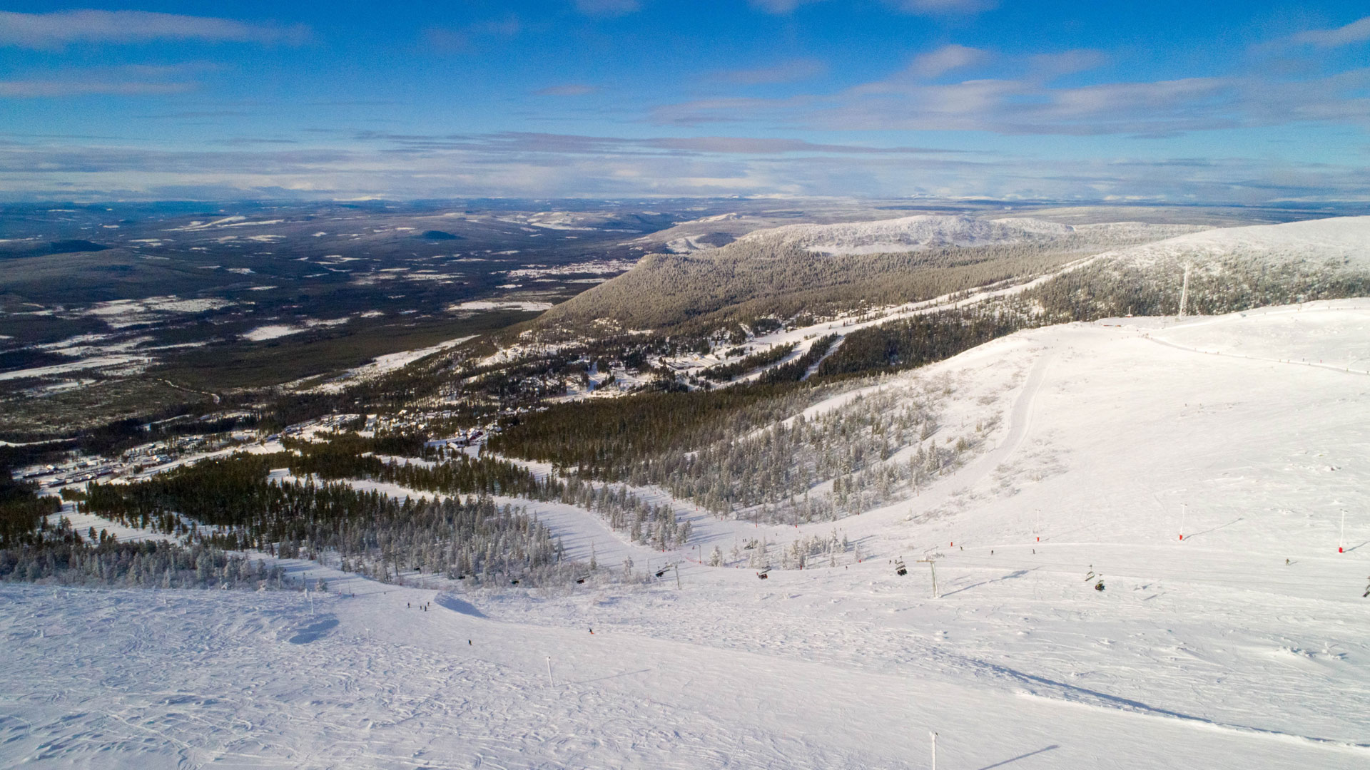 View of a snow-covered mountain landscape in Sweden with forested valleys and a blue sky in the background