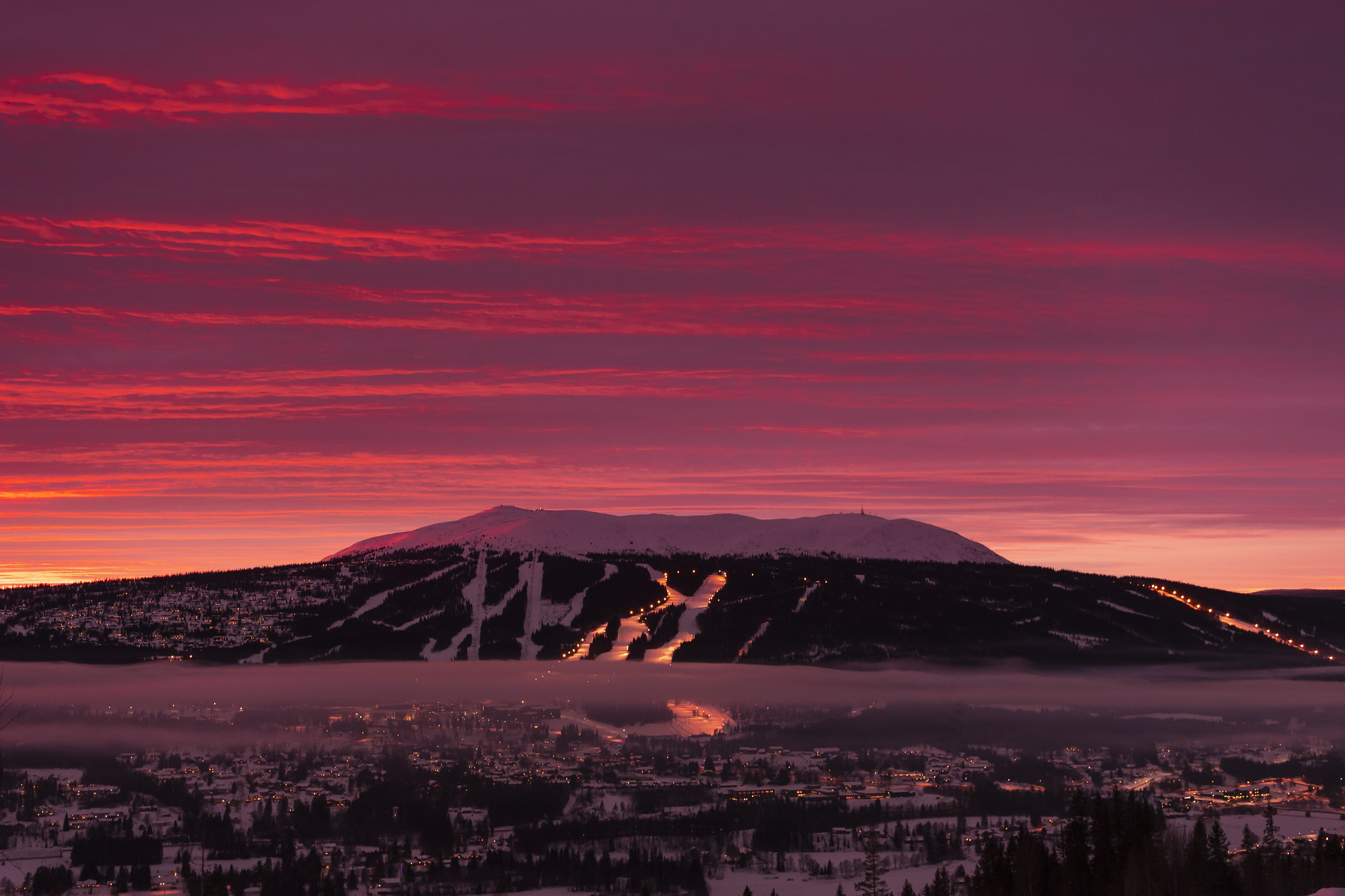 Sunset over snow-covered mountains with lit ski slopes in Trysil, Norway