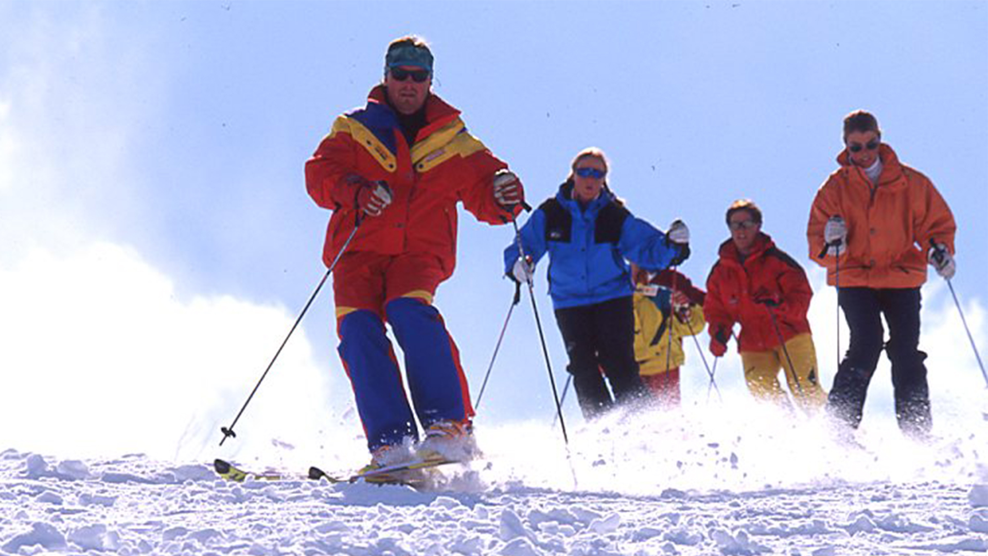 Personer åker skidor i en grupp på en solig snötäckt sluttning
