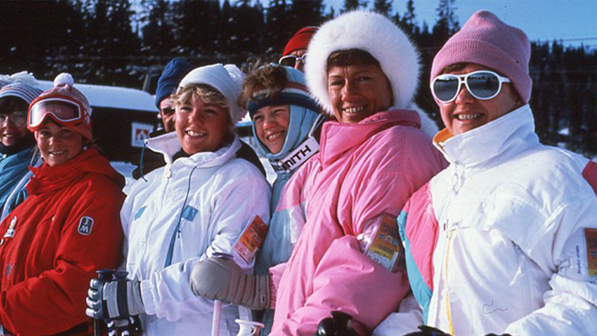 Grupp av leende skidåkare i färgglada vinterkläder, redo för skidåkning i en snötäckt bergsmiljö