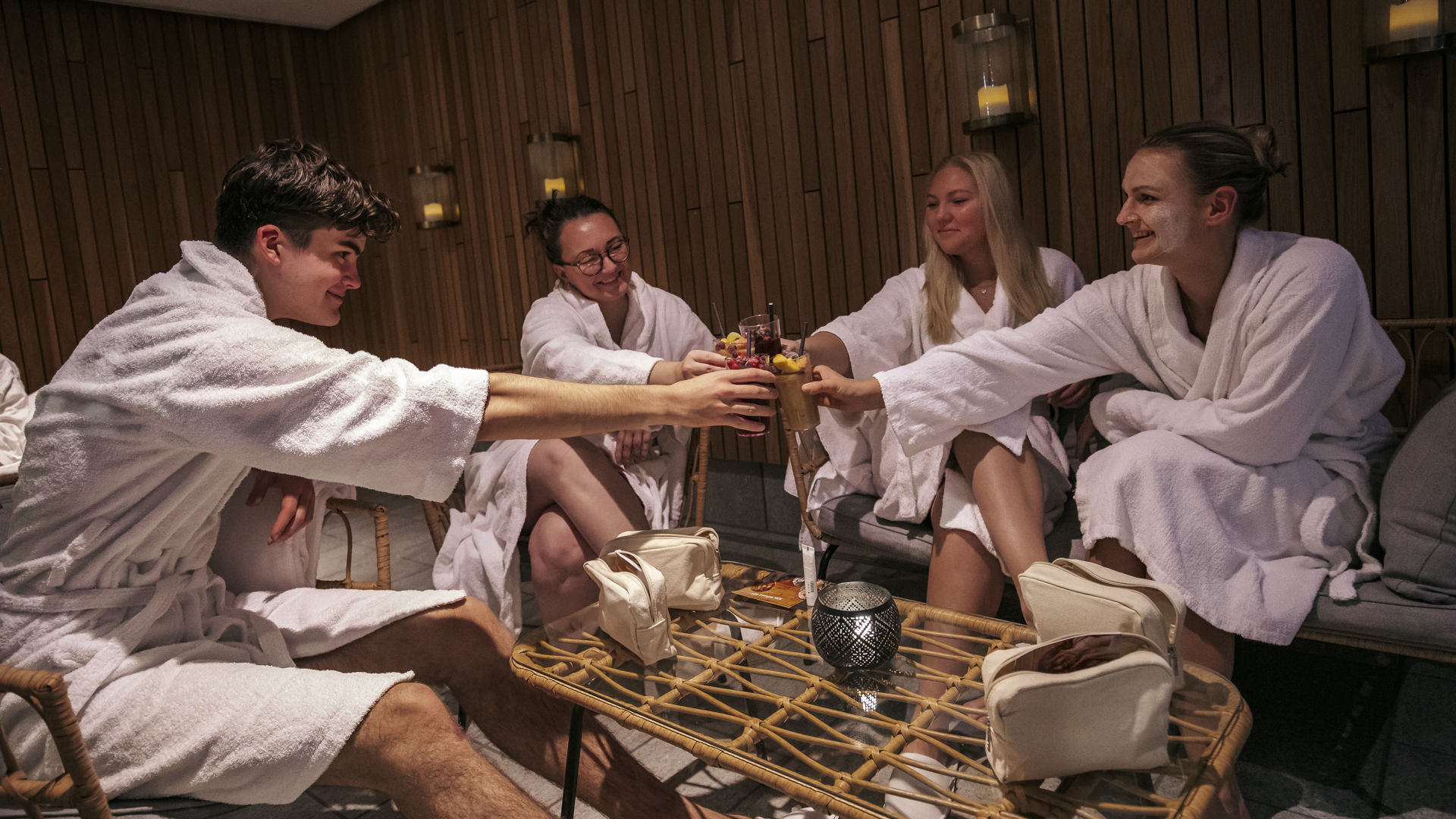 Fyra personer i morgonrockar skålar med drycker i en spa-lounge