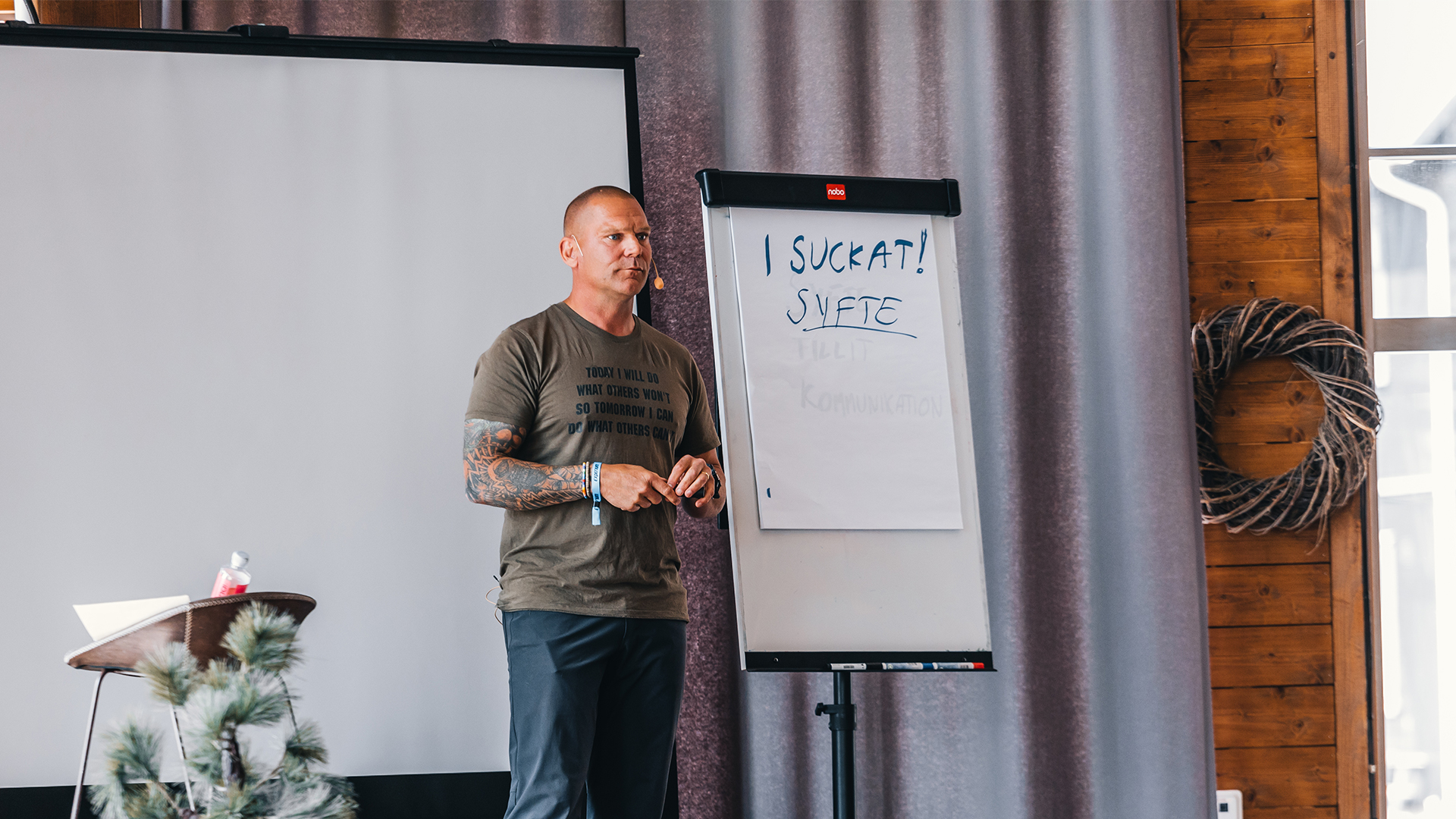 En man håller en presentation vid en blädderblockstavla med texten "I SUCKAT! SYFTE" i ett konferensrum