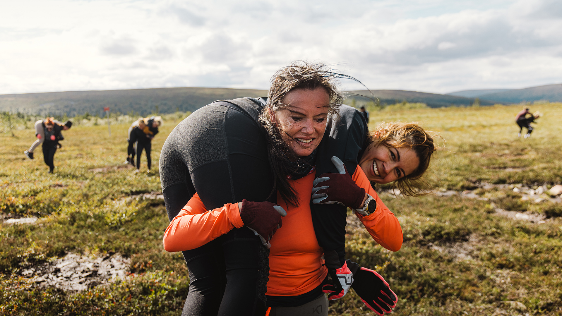 Kvinnor deltar i en hinderbanelopp utomhus på en lerig äng i fjällmiljö