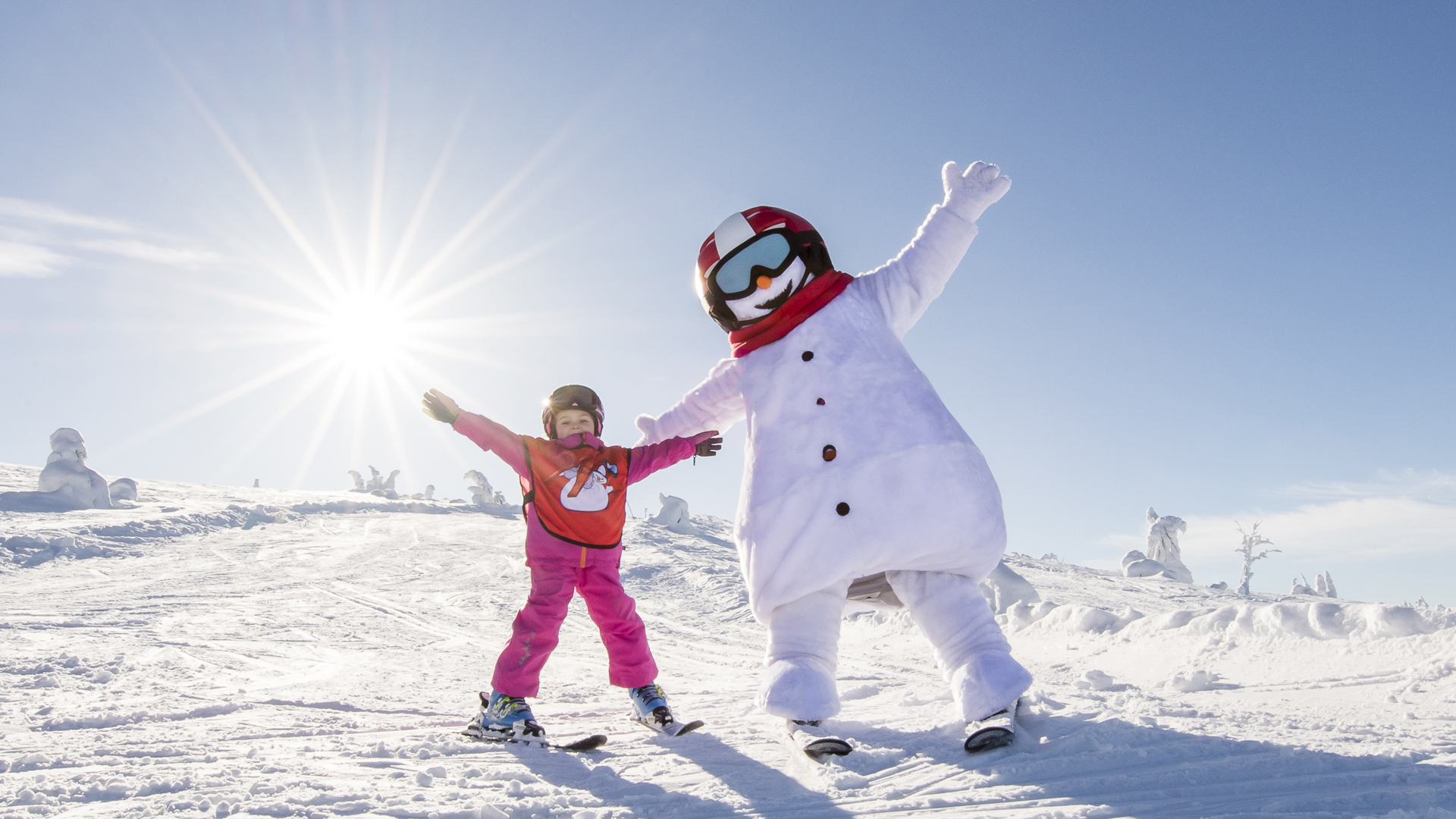 Kinder und Person im Schneemann-Kostüm fahren Ski in sonniger Winterlandschaft