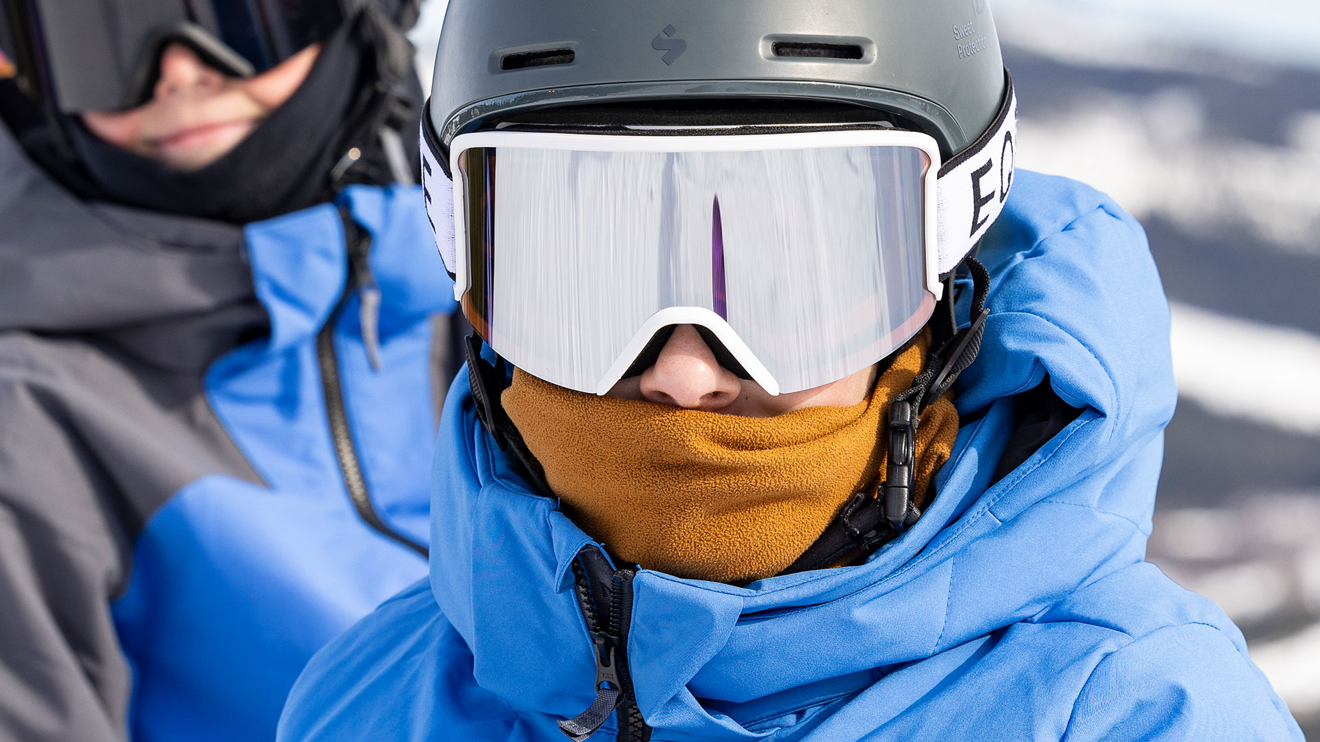 Person i skidutrustning med blå jacka, hjälm och skidglasögon i en snöig miljö