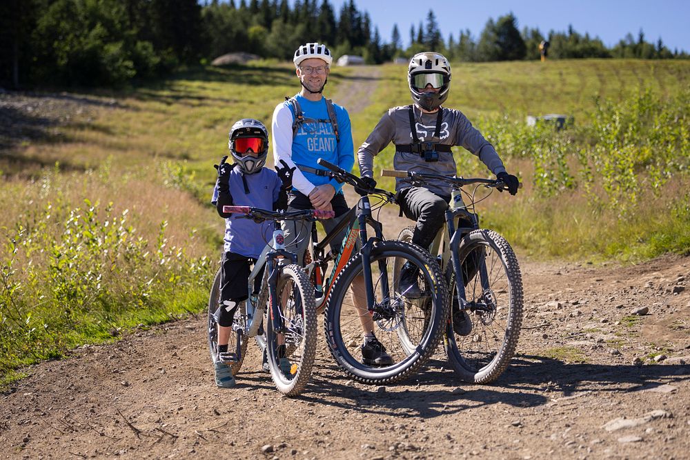 Tre personer med cykelutrustning på mountainbikes i en naturskön park med skog i bakgrunden. En solig dag med klart väder passar för utomhuscykling