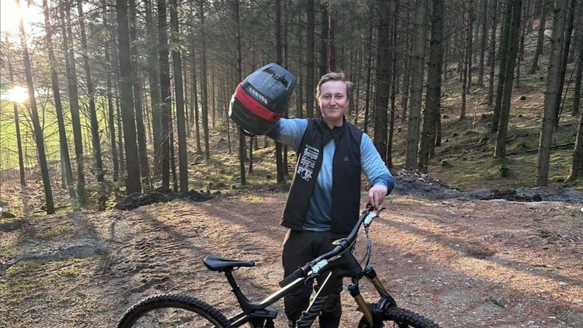 Mand med mountainbike og cykelhjelm i skov, klar til at cykle på stier. Sollys skinner gennem træerne i baggrunden