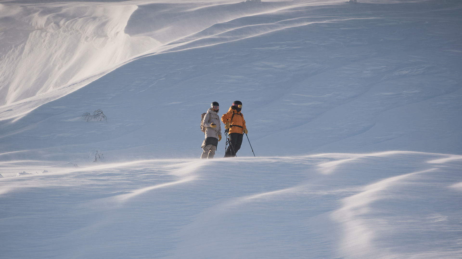 Två personer går på en snötäckt bergssluttning med skidstavar