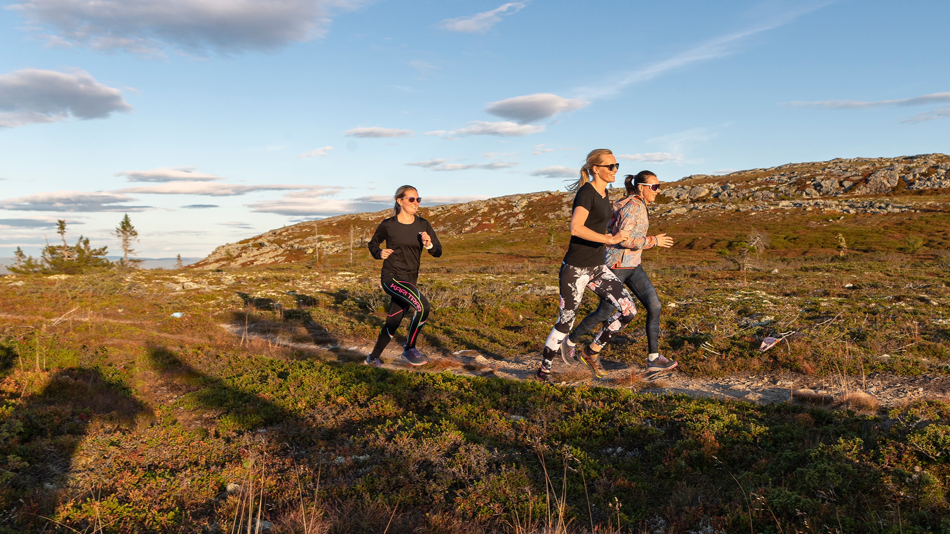 Tre kvinnor joggar i vacker fjällnatur under en solig dag i Sverige
