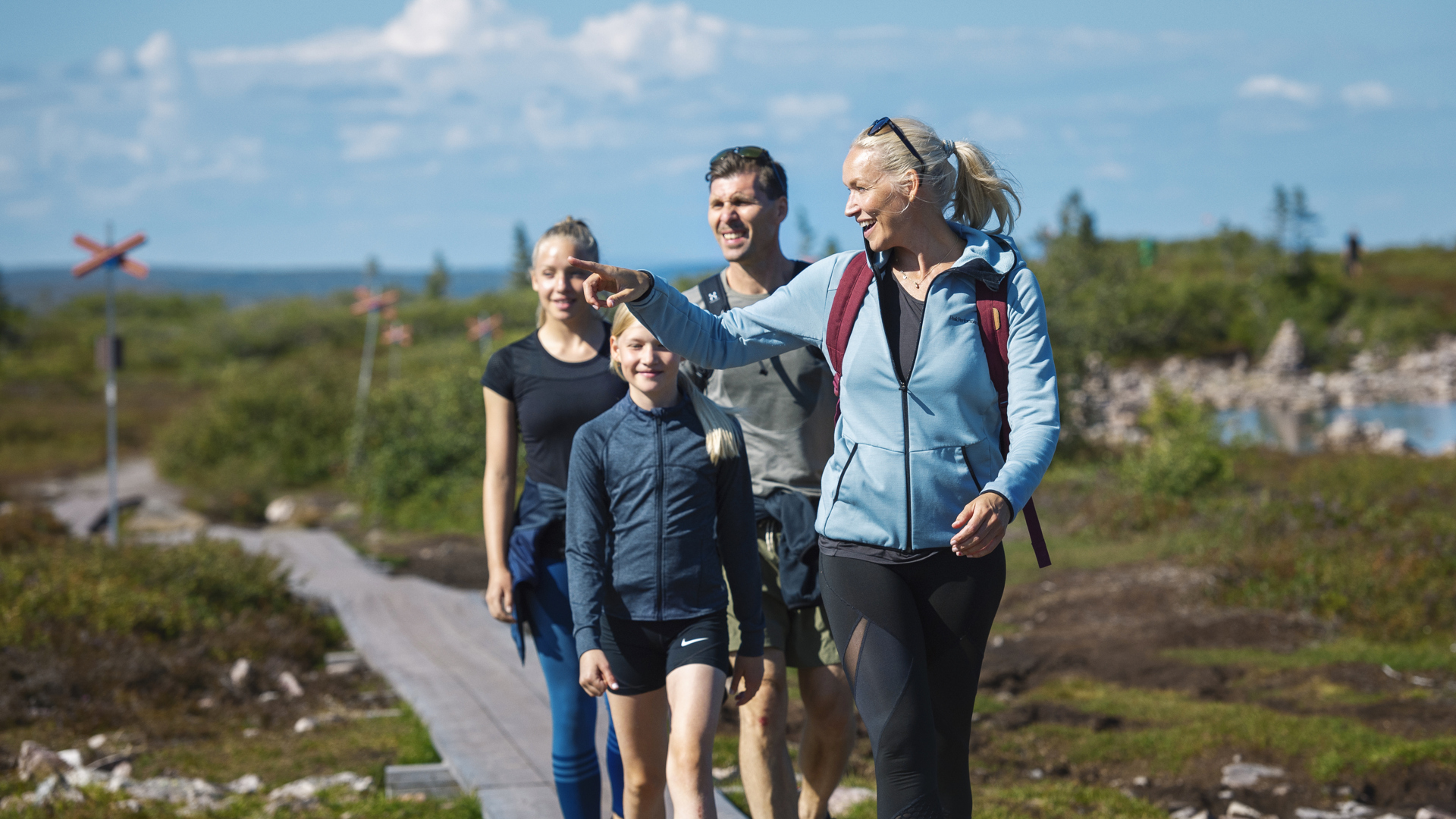Fyra glada vandrare på en stig genom en naturskön fjällmiljö, under en klarblå himmel i Sverige