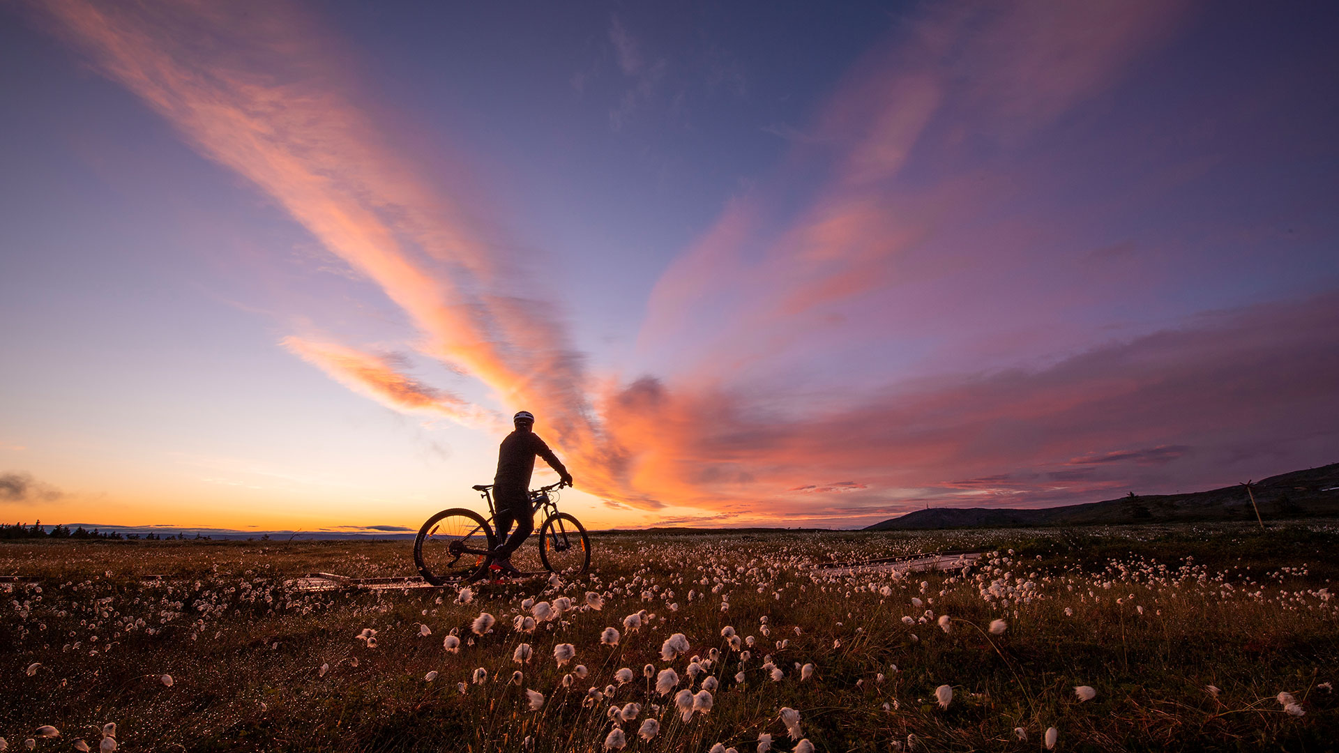 Cyklist på fjället tittar på solnedgång och ett dramatiskt himmelspel.