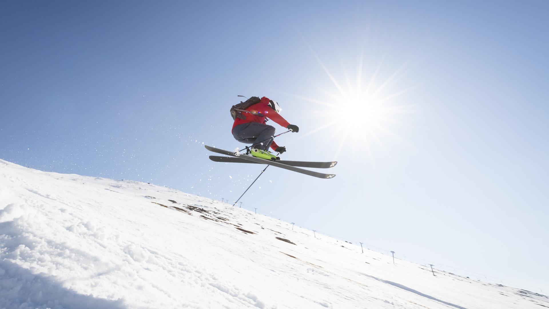 Person som utför ett högt skidhopp på en solig vinterdag, med klar blå himmel i bakgrunden
