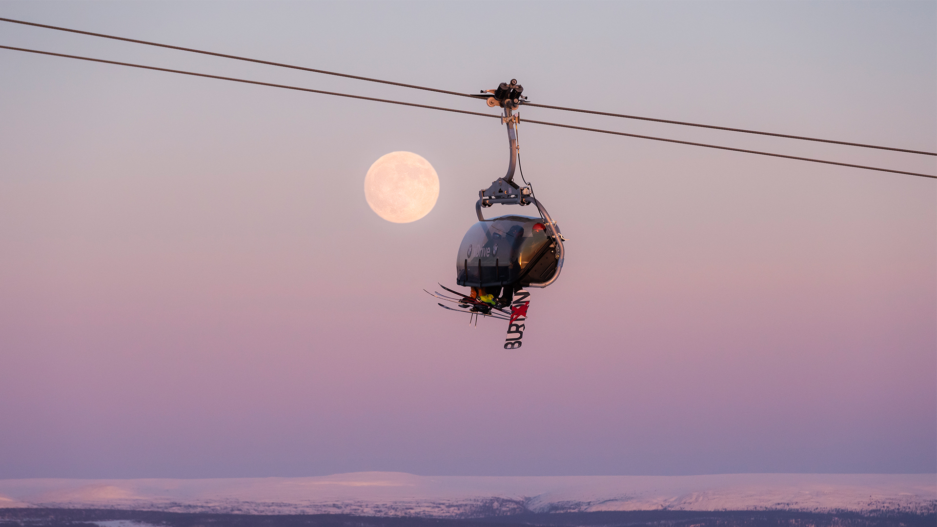 Linbana med åkare i skidutrustning under solnedgång med fullmåne i bakgrunden, pastellfärgad himmel, Lappland, Sverige