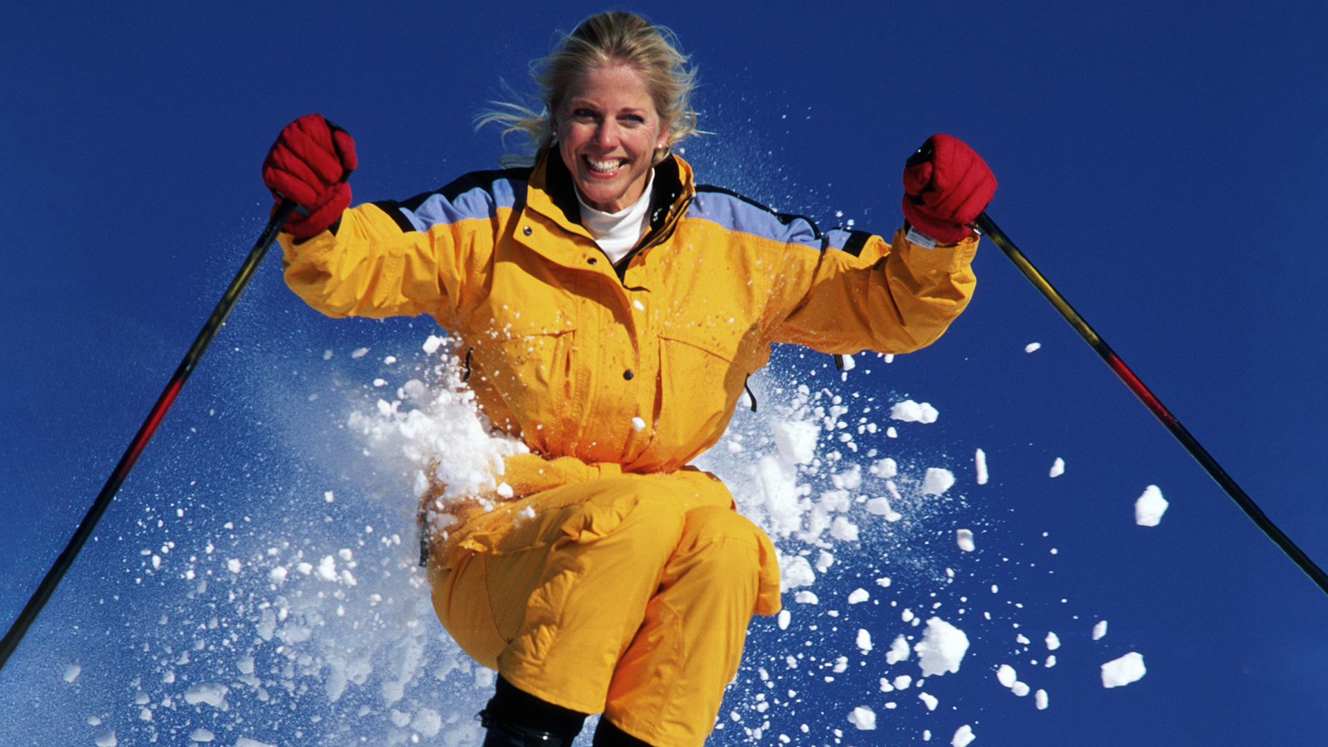 Person åker skidor i färgglad gul jacka, med röd himmel och snö som virvlar runt