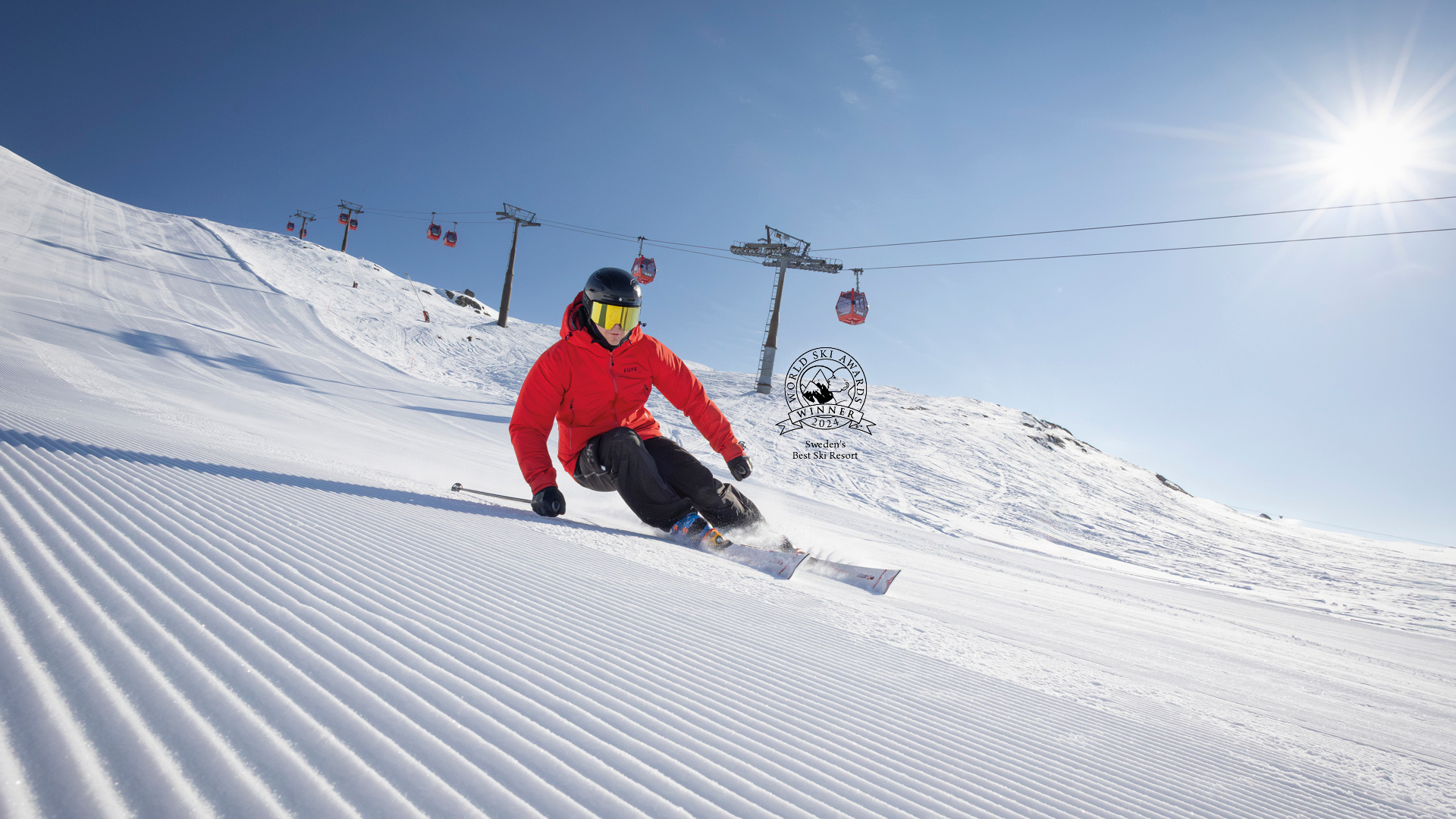 Person skidåkning nedför en pist i soligt väder, med skidlift och klara blå himmel i bakgrunden, i en välpreparerad skidbacke