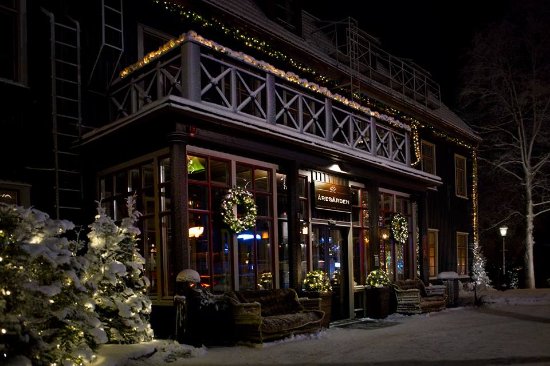 Beleuchtete Fassade des Restaurants, dekoriert mit Weihnachtsbeleuchtung und Kränzen, umgeben von schneebedeckten Bäumen, in der Winternacht