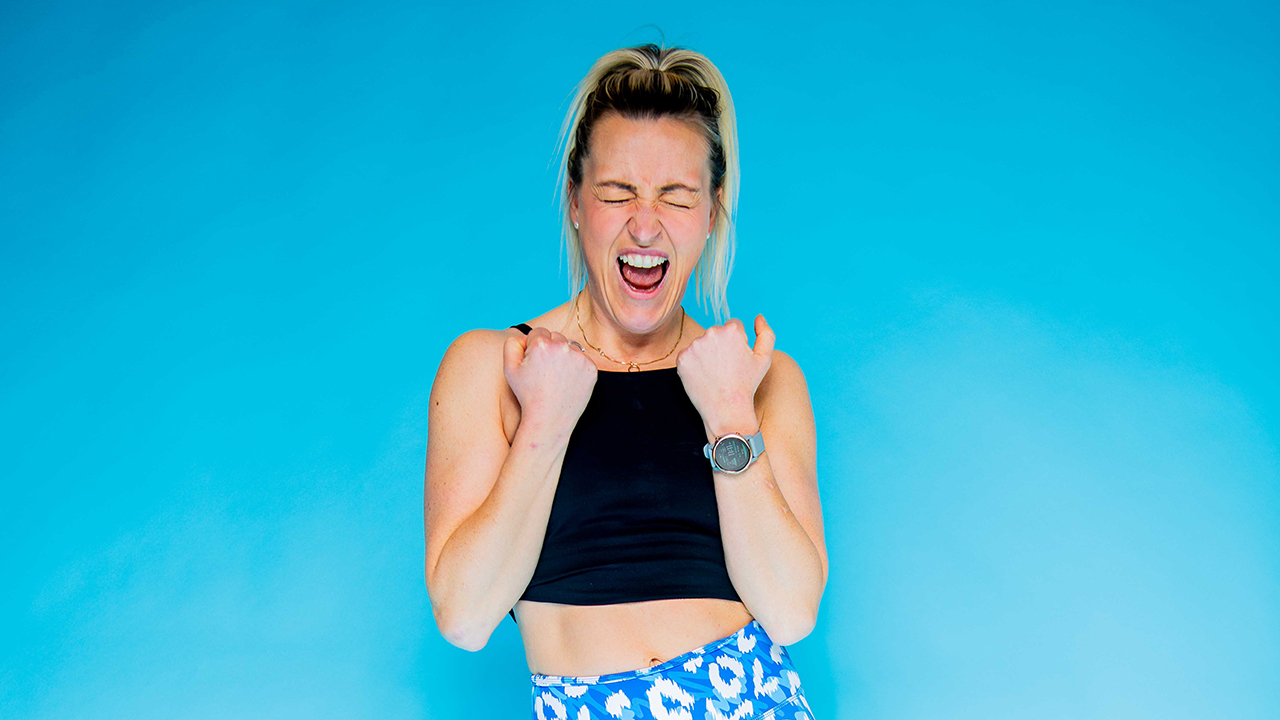 Kvinne i treningsklær viser seiersgest med blå bakgrunn