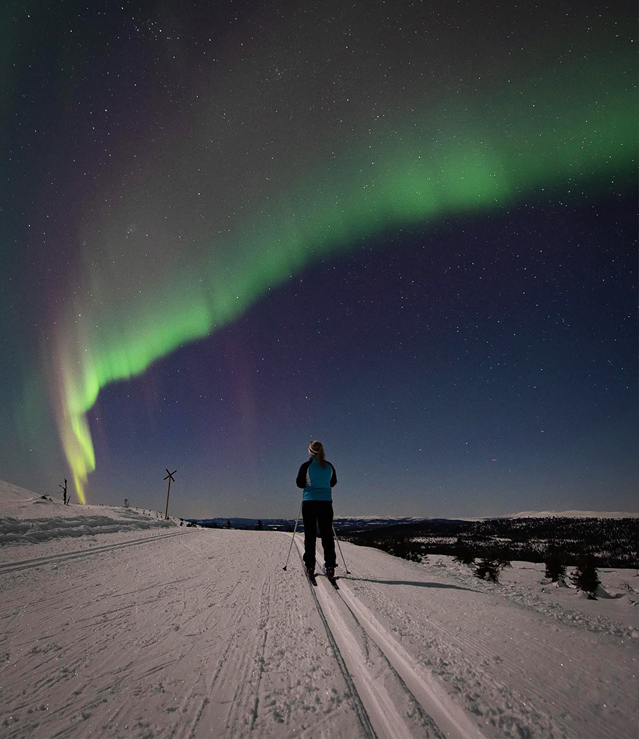 Person skiing at night under the vibrant northern lights on a snowy landscape