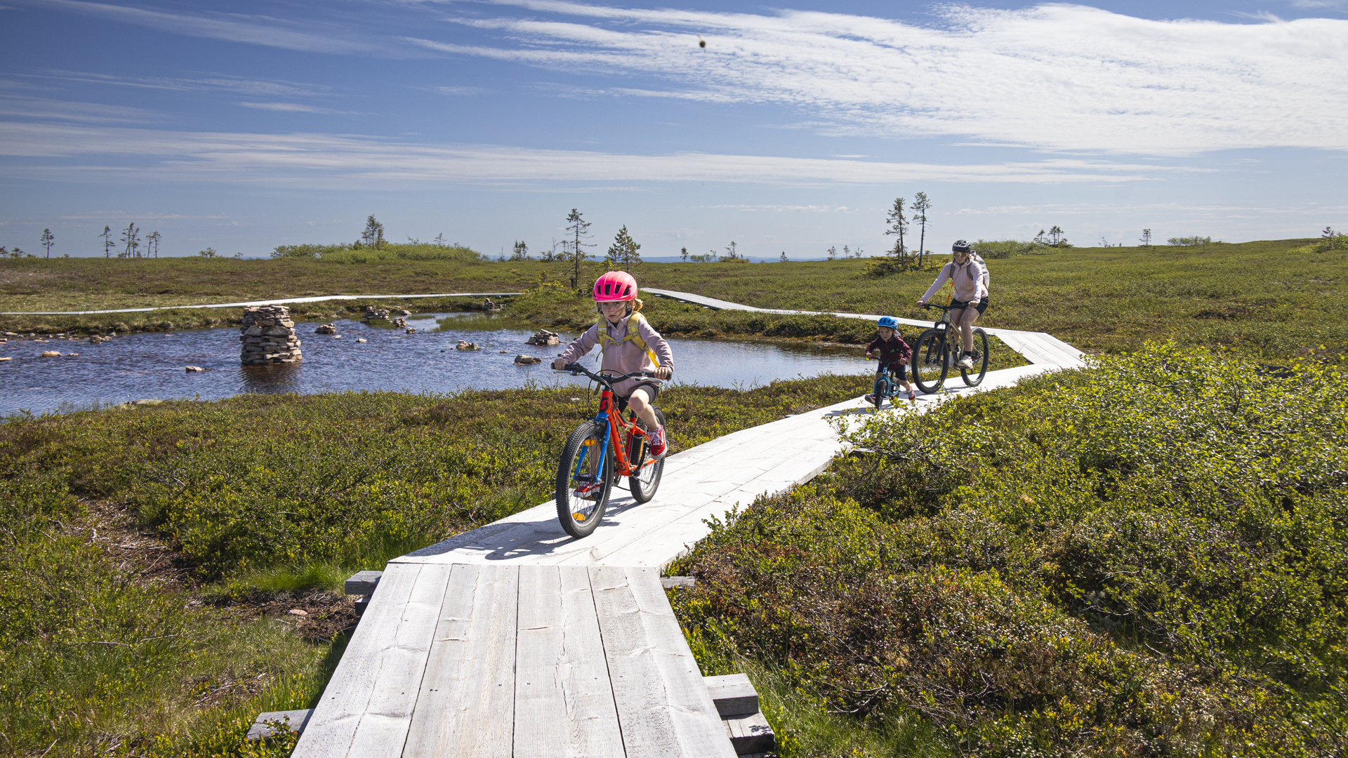 En mor og to barn som sykler på treklopper i Sälen under deres sykkelferie. Klar himmel og fin utsikt.