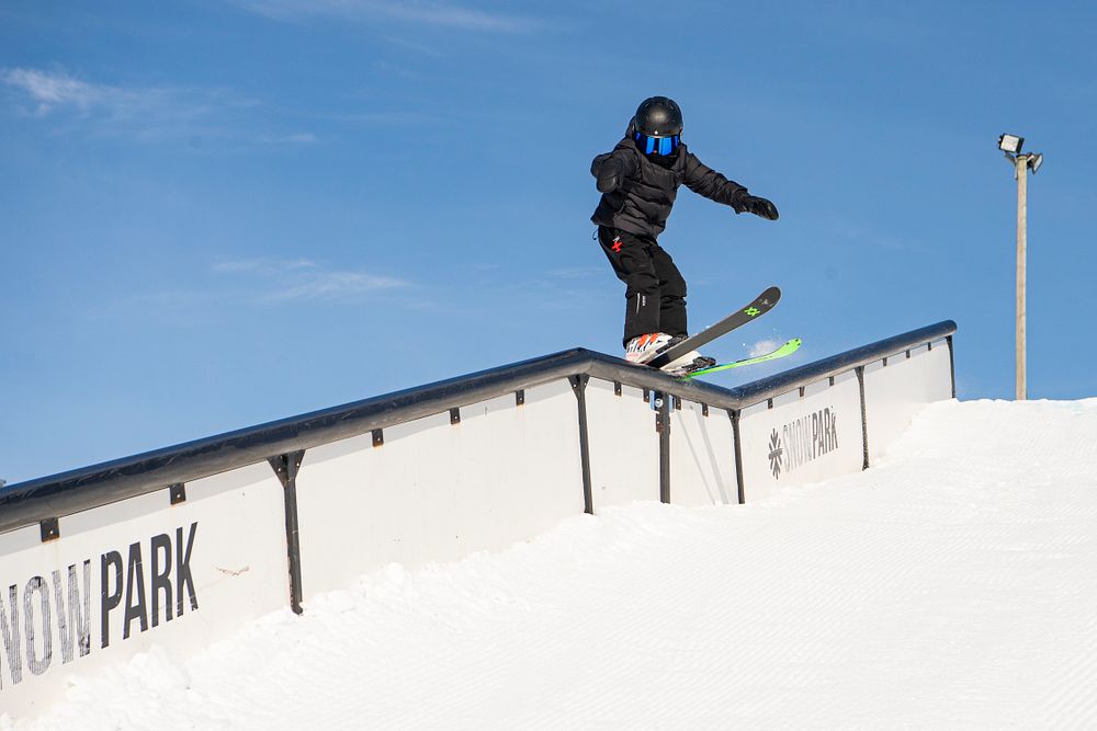 Person åker snowboard på rail i en snöpark under klarblå himmel