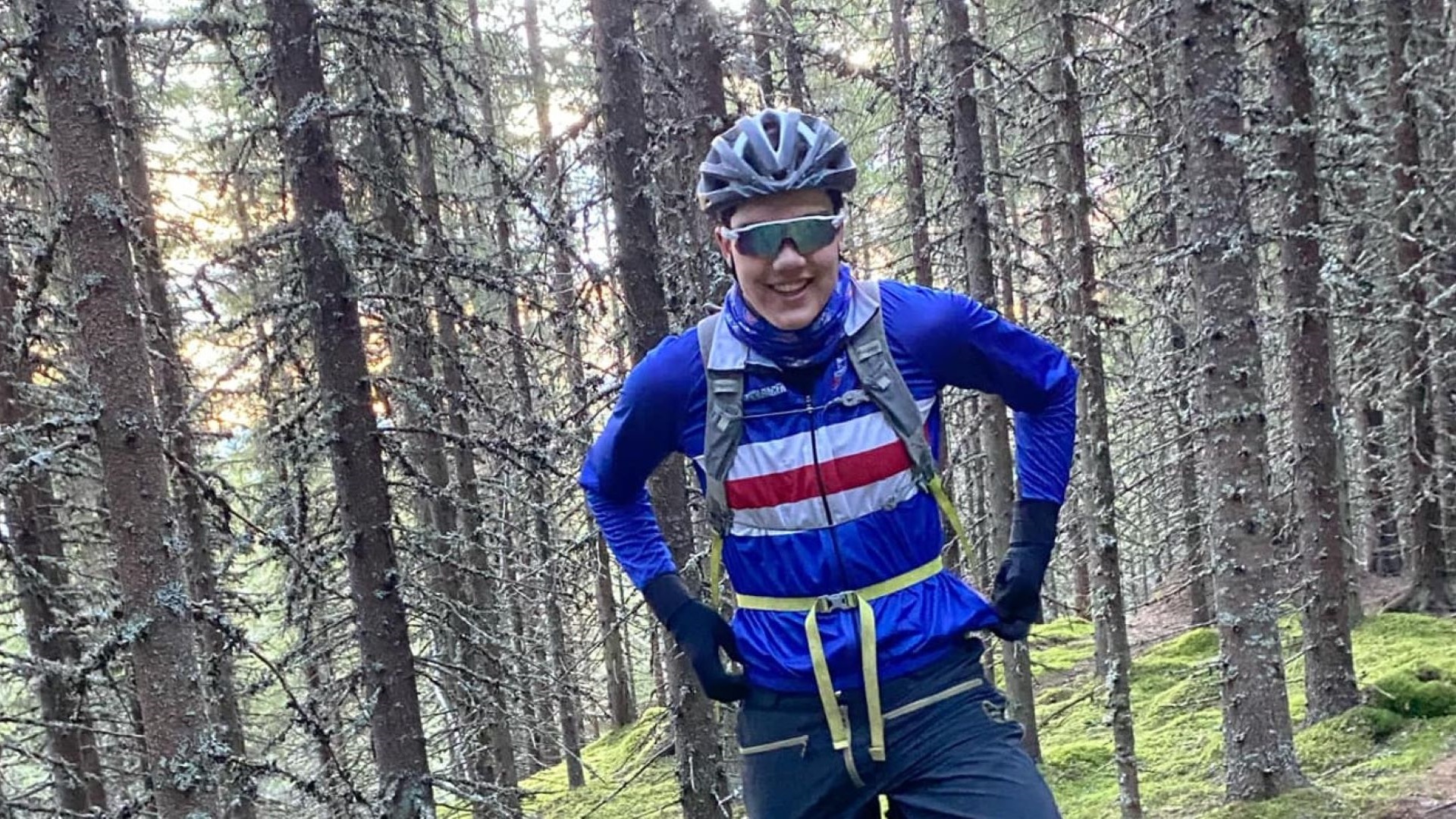 Person iført cykelhjelm og sportsbriller står i en skov i lysende sportsbeklædning