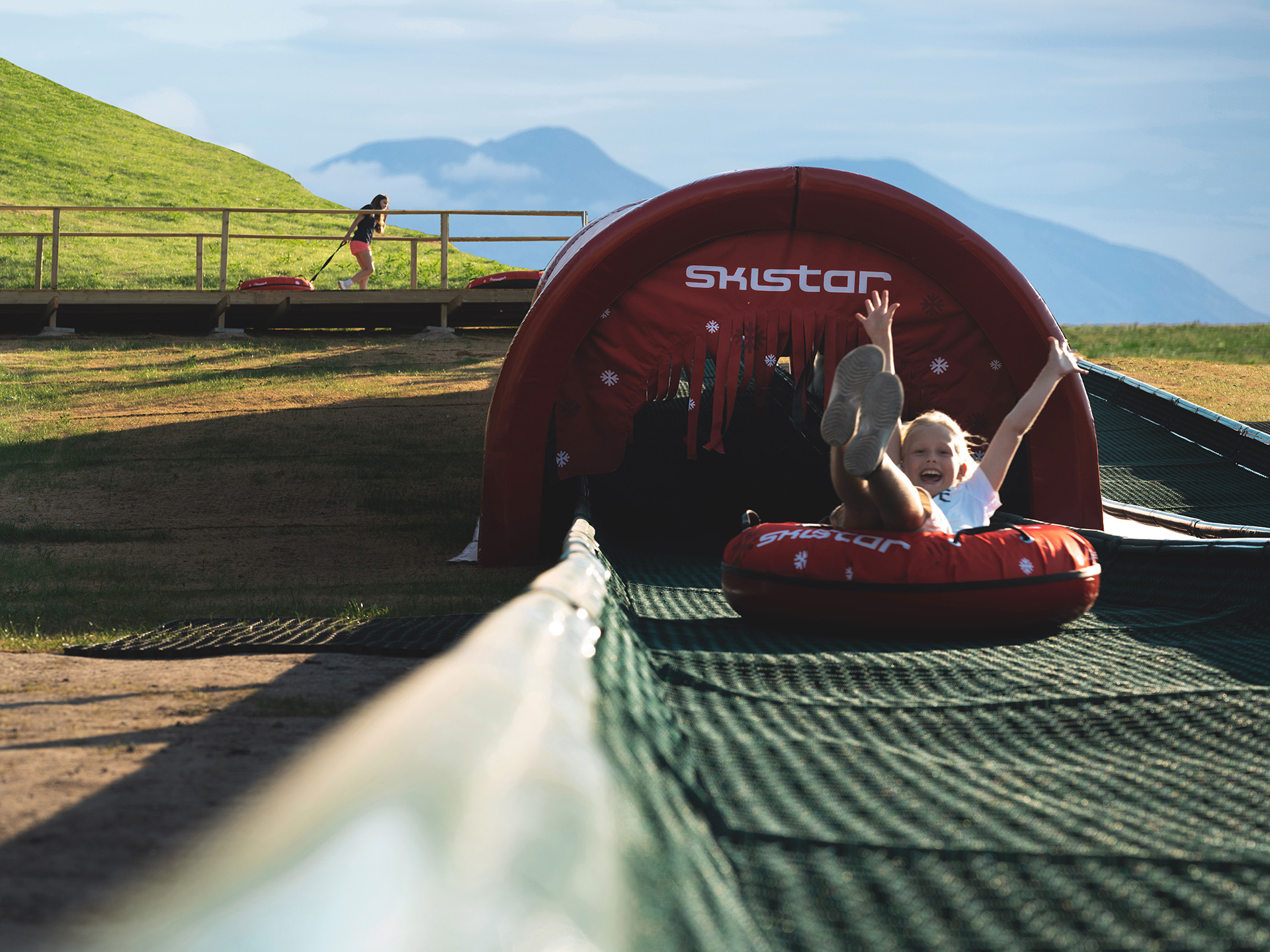 Barn åker rodel i en uppblåsbar ring på en grön sommarbacke vid en skidresort
