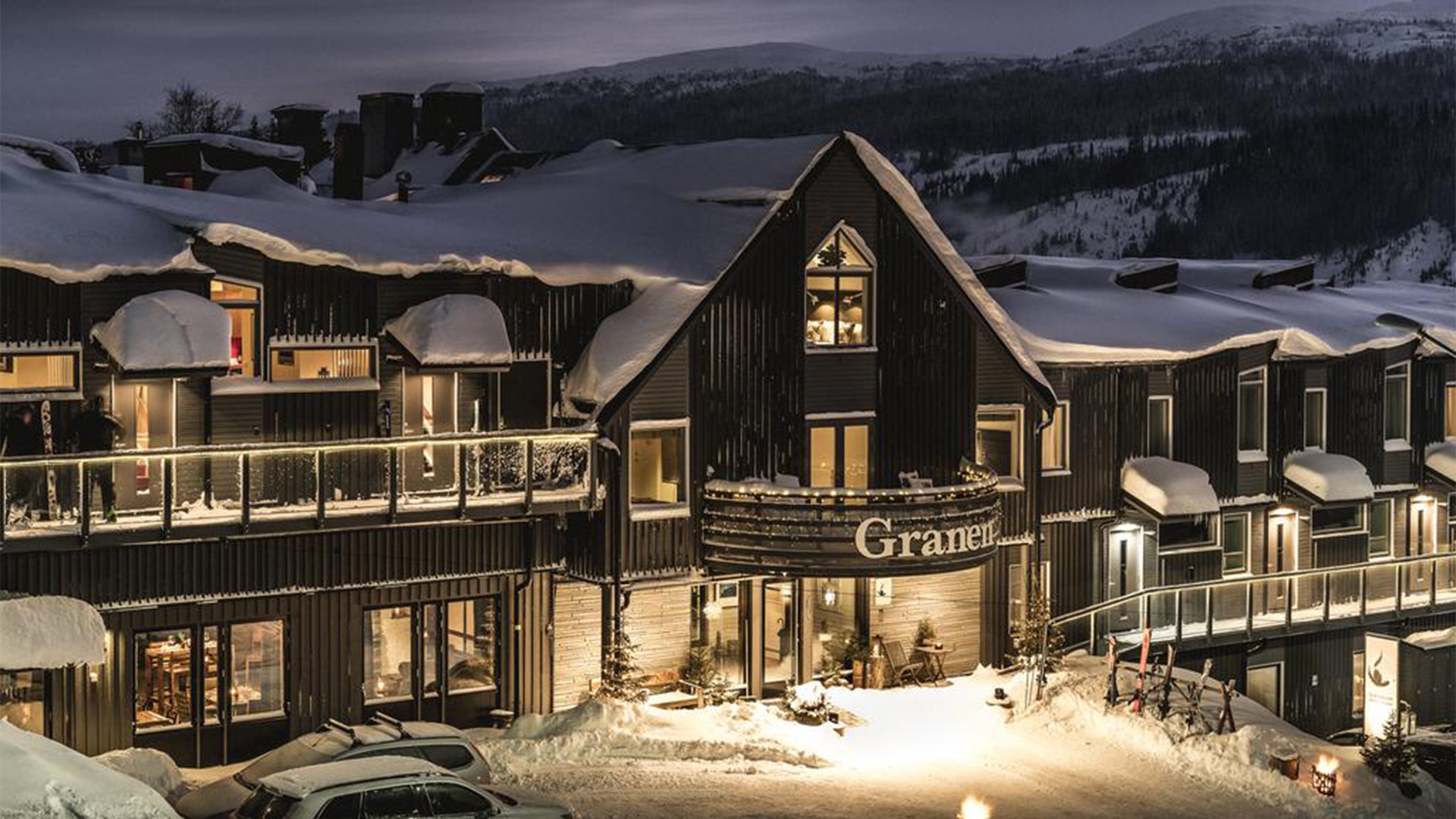 Vintrigt hotell Granen i snötäckt bergsområde, upplyst på kvällen med berg i bakgrunden