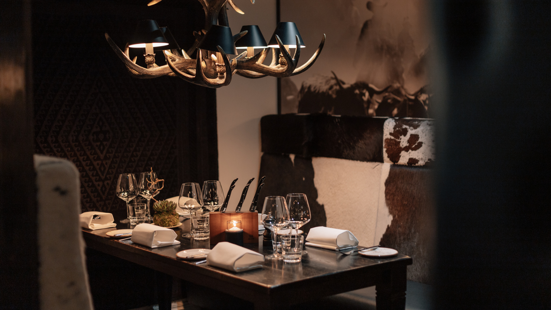 Elegant dukning på en mysig restaurang med rustik interiör, inklusive hornformad ljuskrona och stilfulla bordsdekorationer