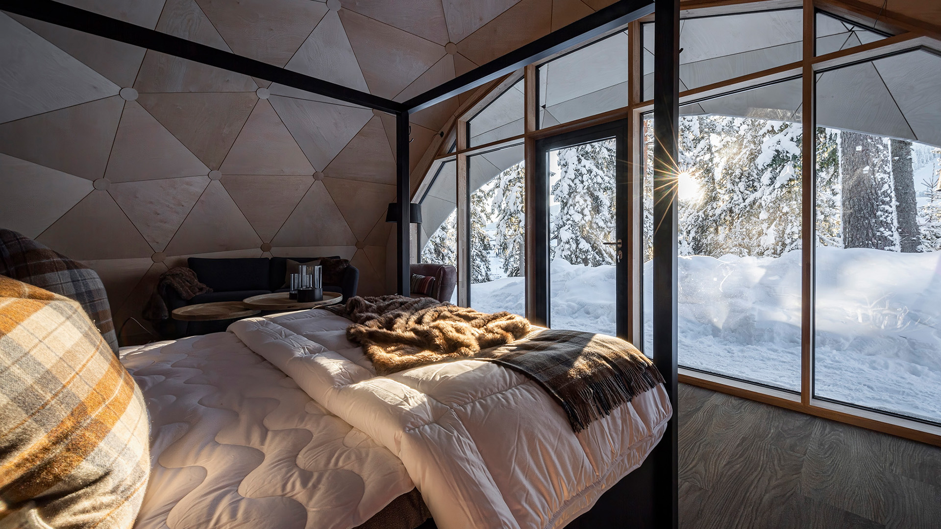 Sovrum i kupolformad stuga med stora fönster som vetter mot snötäckt skogsutsikt