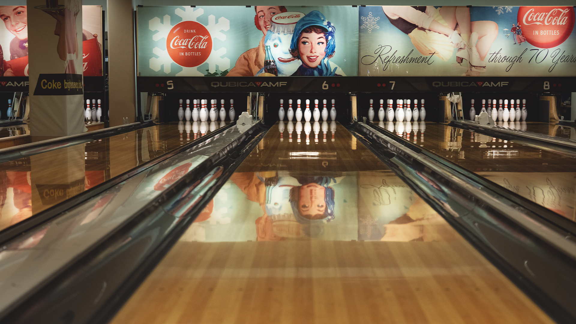 Bowlingbane med vintage Coca-Cola-reklame på veggene i bakgrunnen, viser oppstilte kjegler og blankpolerte baner