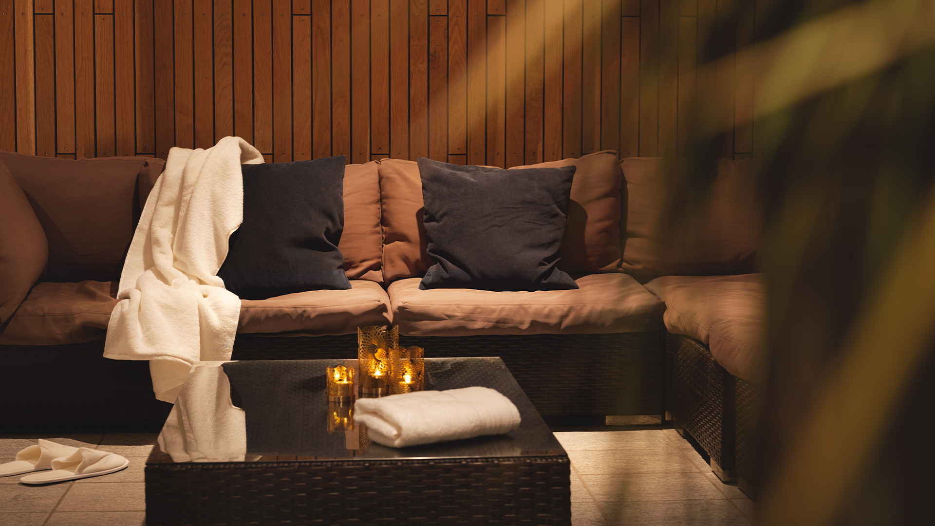 Avslappende spa-lounge med komfortable sofaer, tepper og tente lys i et varmt, trebekledd miljø