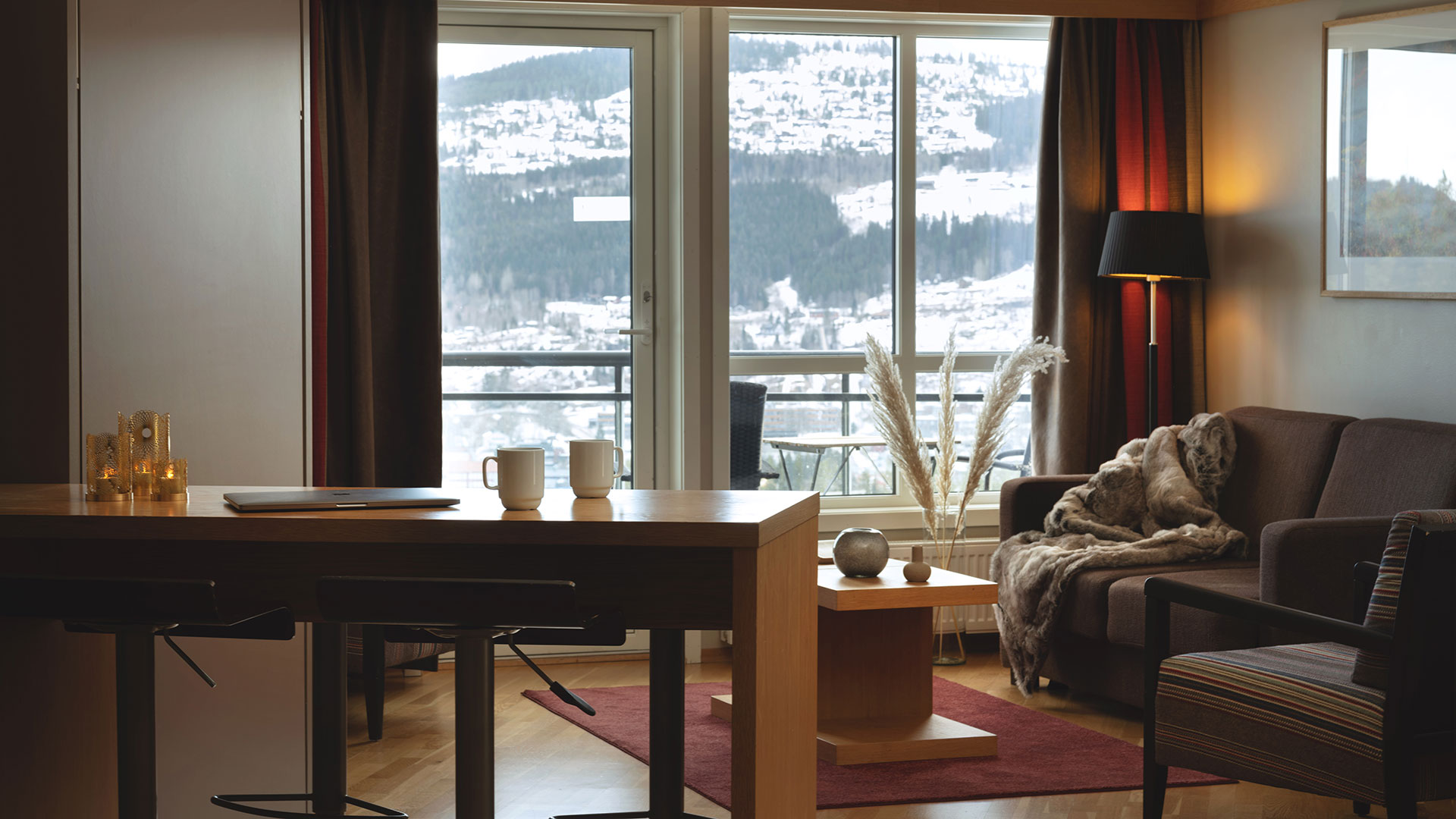 Modernt vardagsrum med utsikt över snöklädda berg, inrett med soffa, golvlampa och kaffebord