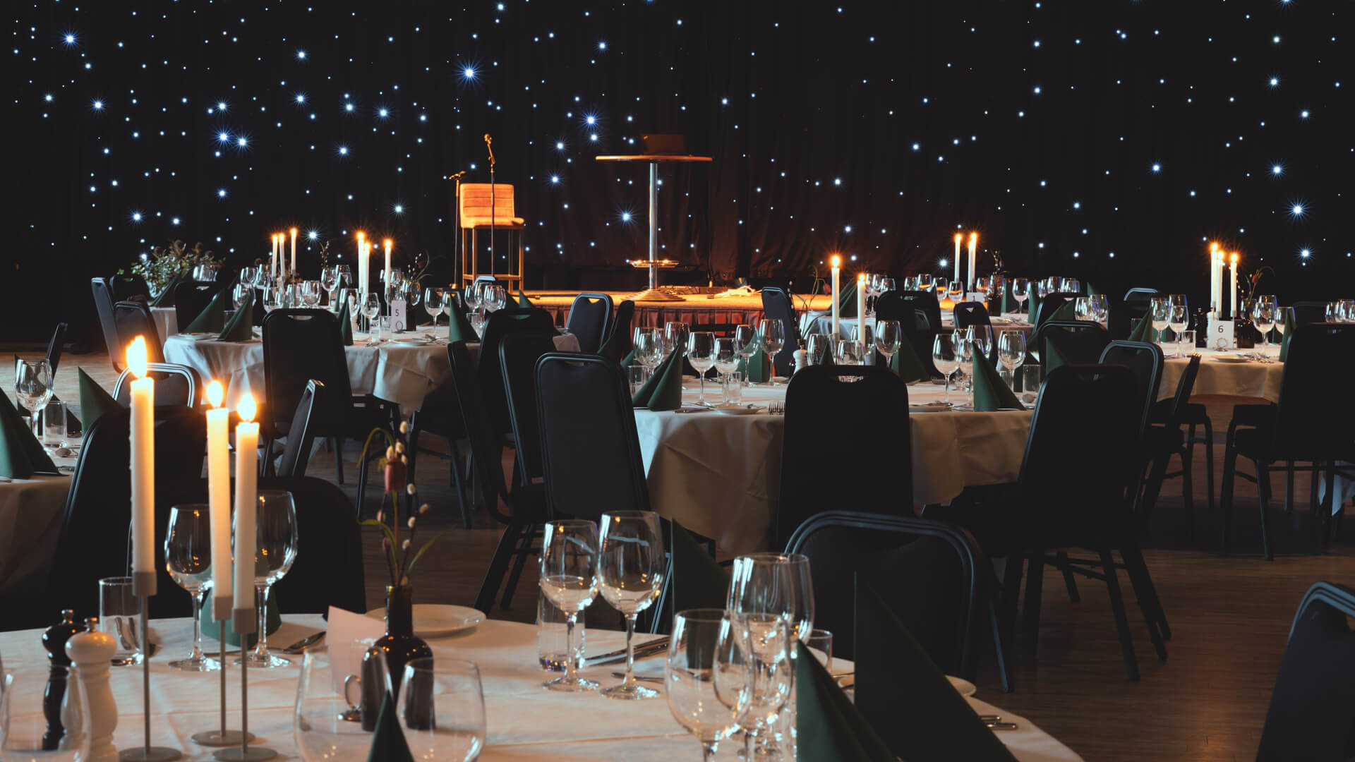 Festsal med dekkede bord, tente lys og en scene i bakgrunnen