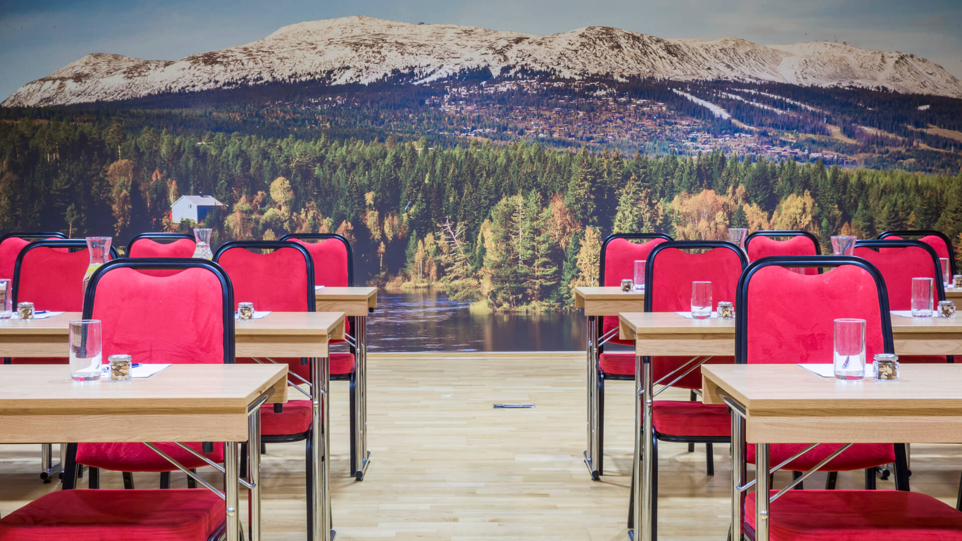 Møterom med røde stoler og trebord, utsikt over en fototapet med skog og fjell i det fjerne