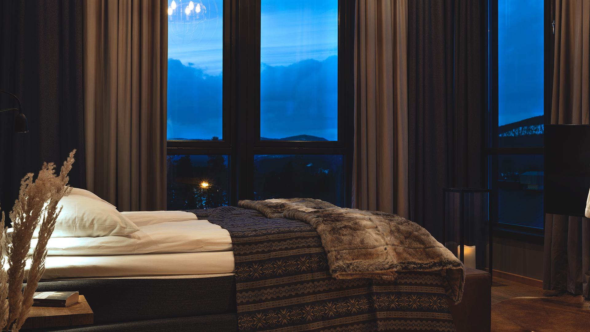 Luksuriøst soverom med utsikt over nattehimmelen, dobbeltseng med mønstret sengeteppe og pelspledd, store vinduer med gardiner