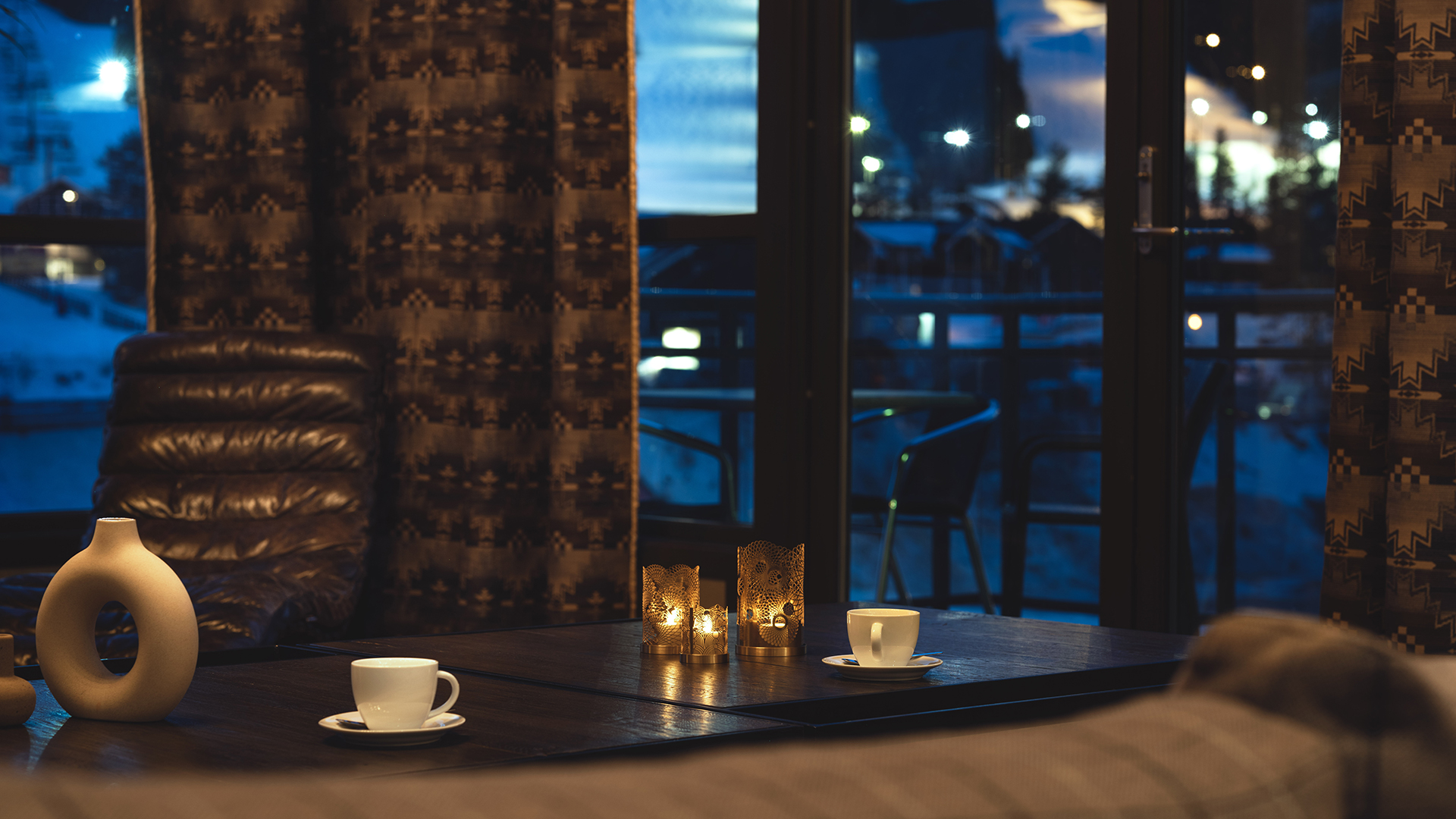 Avkopplande interiör med två koppar kaffe på ett bord framför en fönstervy av en kvällsbelyst balkong