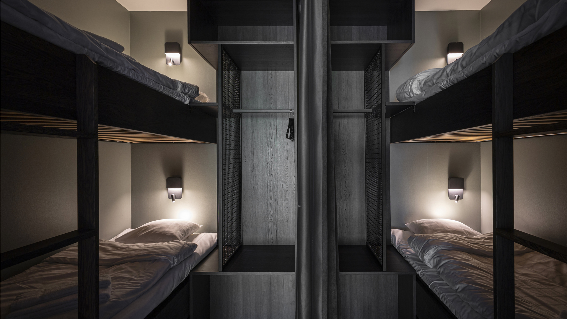 Fyra moderna våningssängar i minimalistiskt designad sovsal, med stämningsfull belysning och neutrala färgtoner