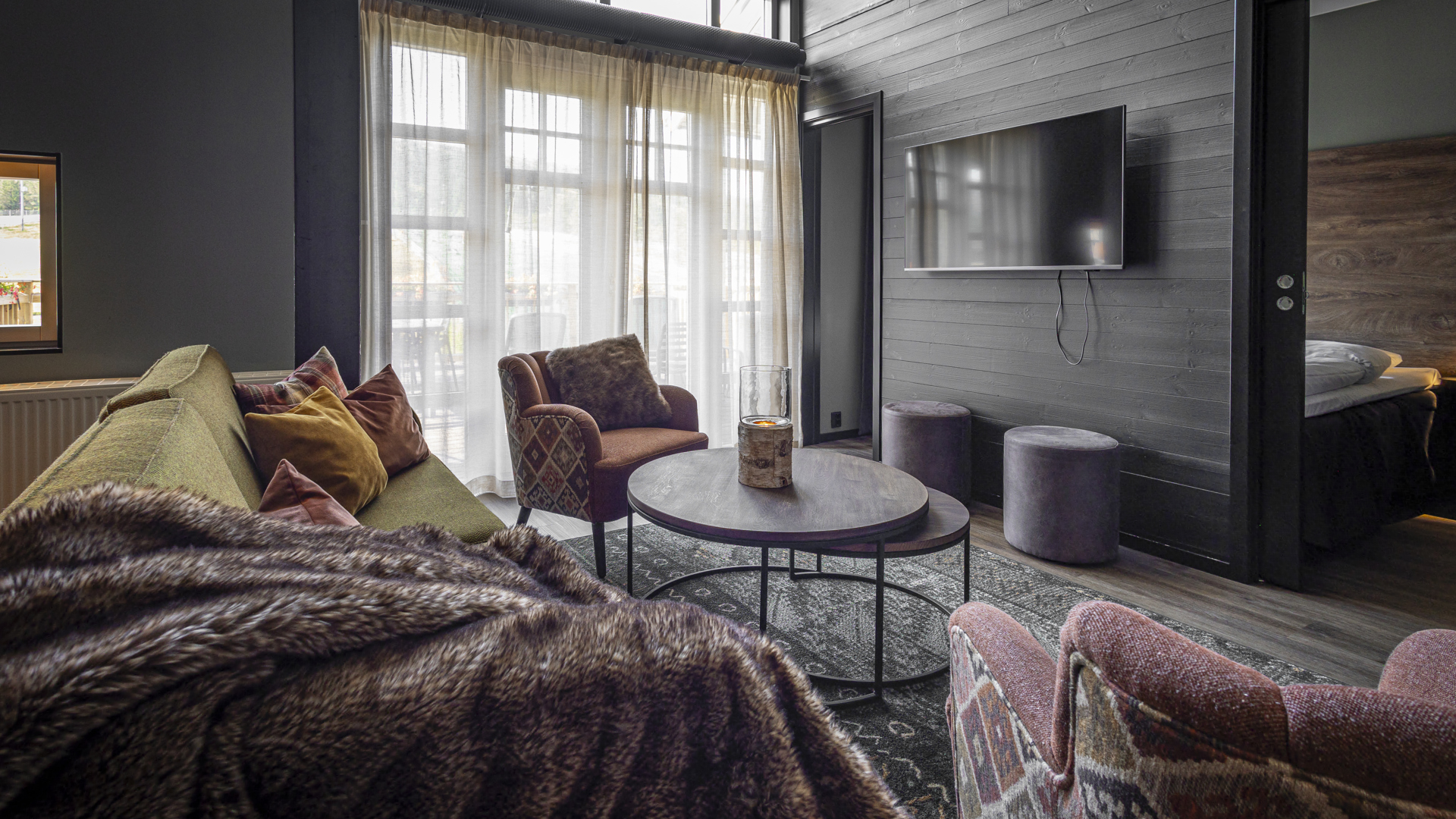 Modern och mysigt vardagsrum med grön soffa, flerfärgade kuddar, rund bord, TV och stora fönster med skira gardiner, som skapar en inbjudande atmosfär