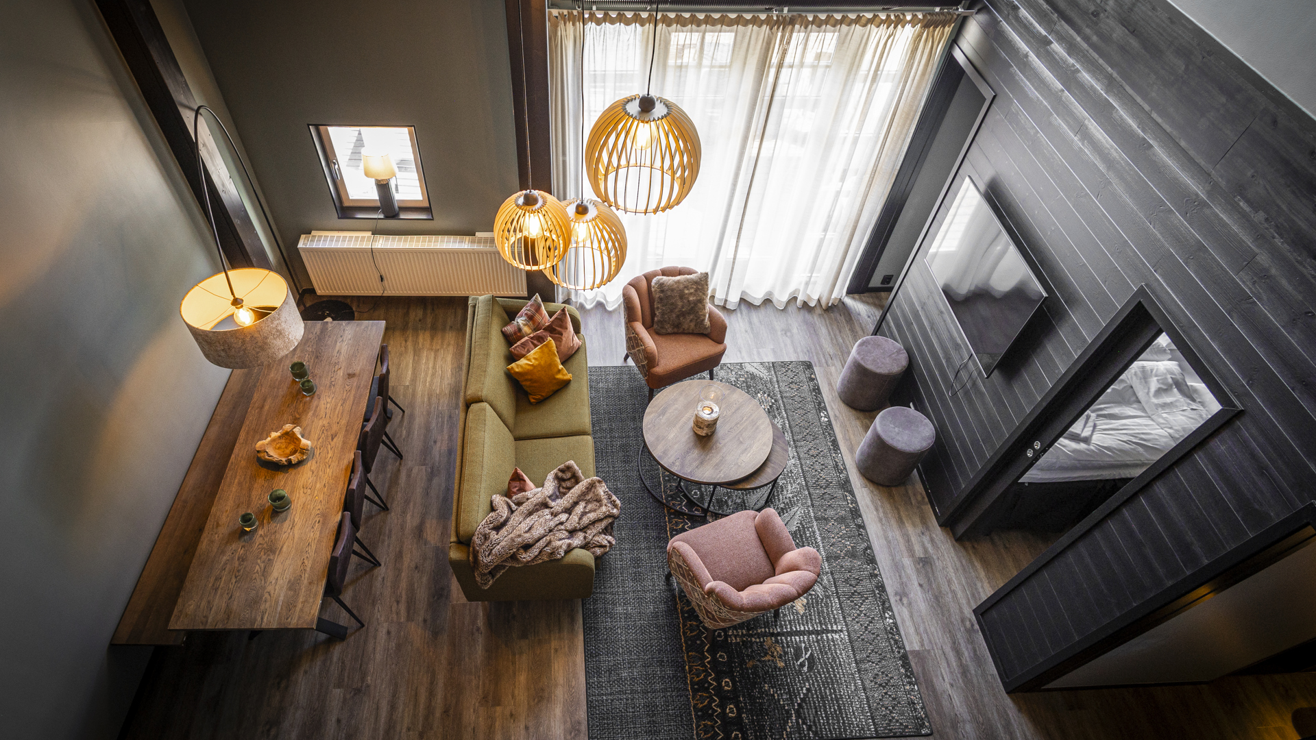 Luftig modern vardagsrum med stilren inredning, sett från ovan. Mörkt trägolv, grön soffa, runda bord och dämpad belysning