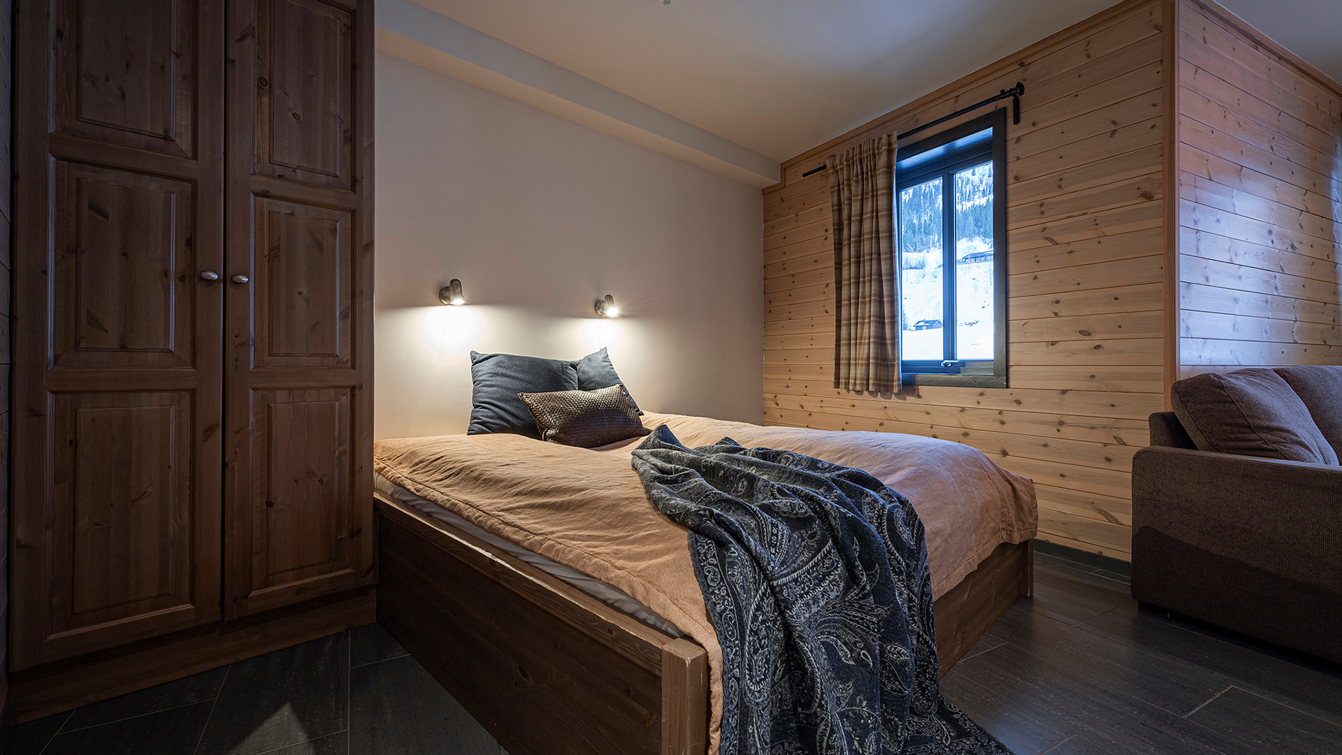 Sovrum med dubbelsäng, träpaneler på väggarna, garderob och fönster med gardiner, mysig inredning