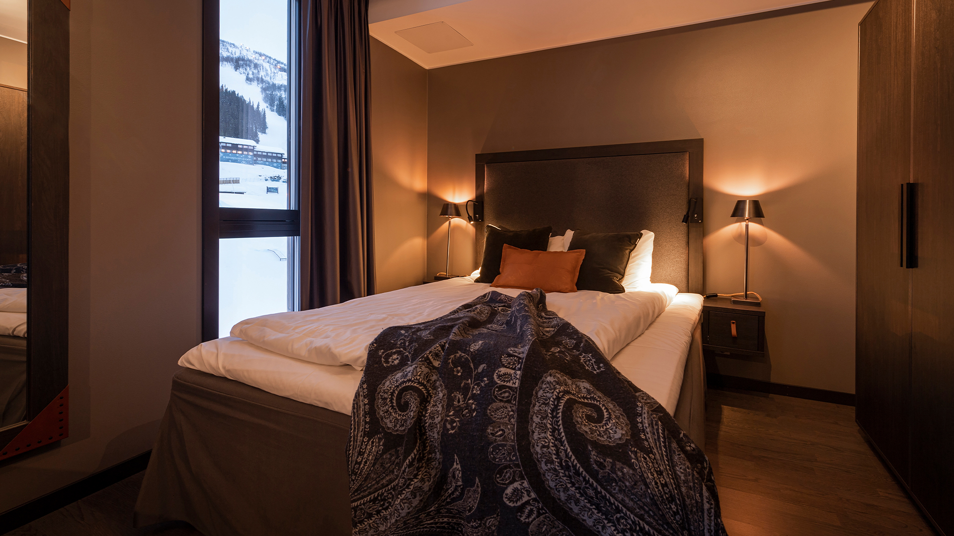 Snygg och bekväm hotellrum med dubbelsäng och stämningsfull belysning. Stort fönster erbjuder utsikt över snöiga berg