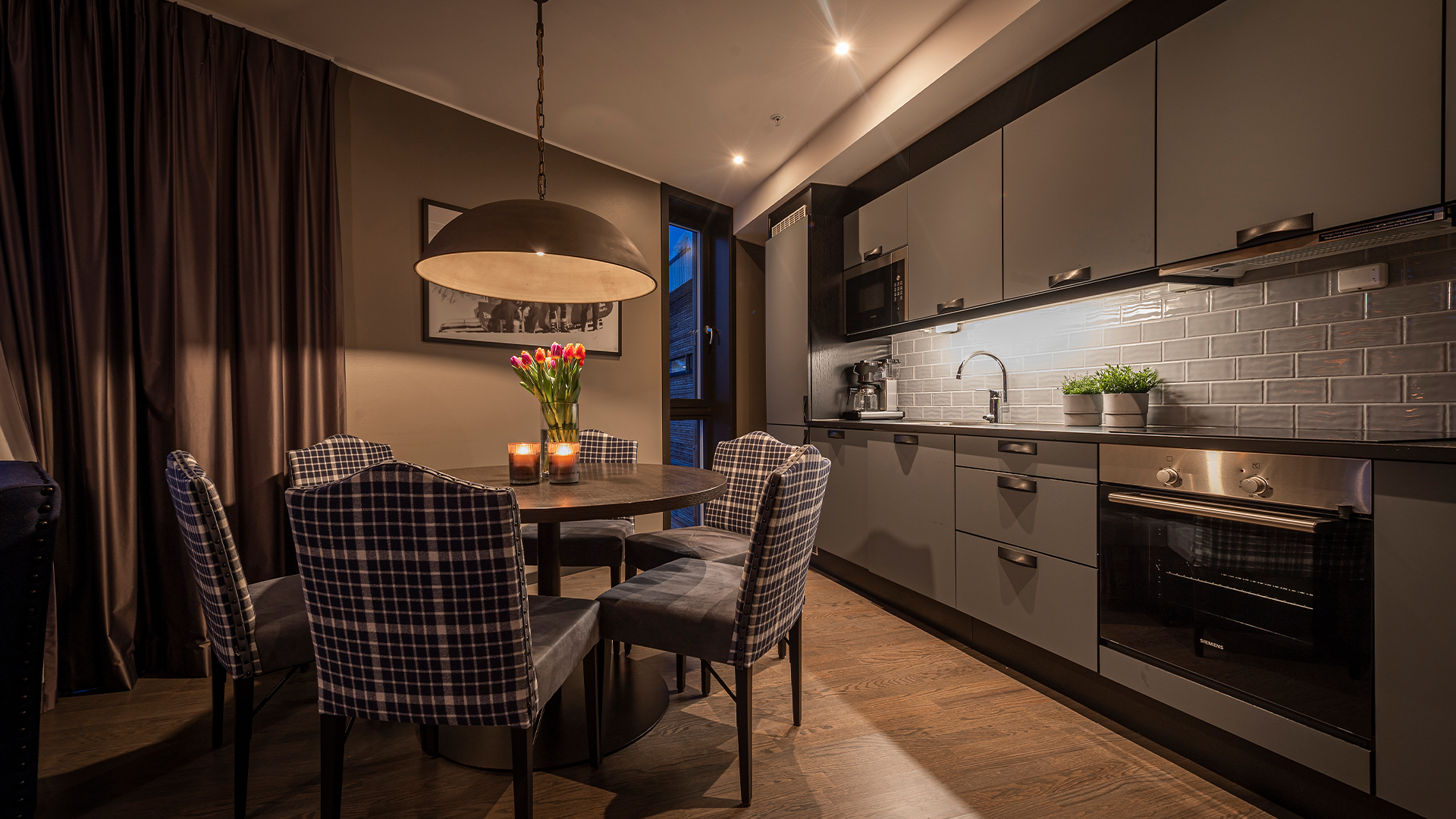 Modernt kök med grå skåpluckor, matbord med rutiga stolar, hängande taklampa och fräscha tulpaner i en vas