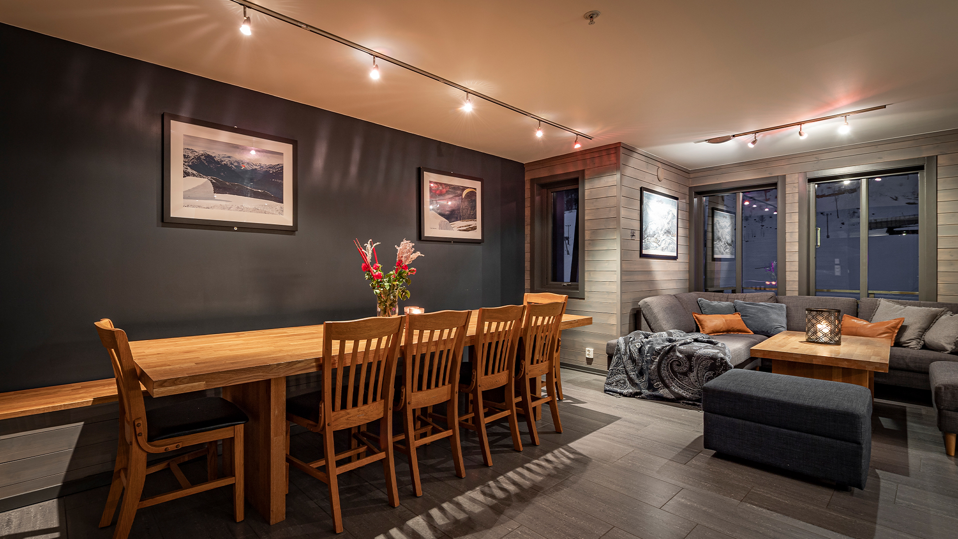 Modernt vardagsrum med träbord, sex stolar och grå soffa, inrett med blommor och konstverk på väggarna