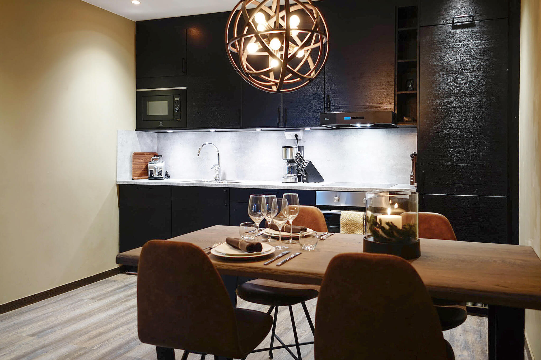 Modernt kök med mörka skåp och trädetaljer, elegant middagsdukning på rustikt matbord, stilfull belysning ovanför